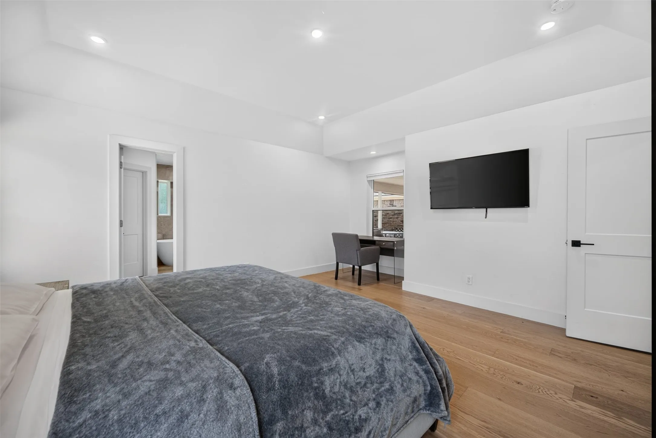 Bedroom with light wood-finish flooring, recessed lighting, and a white flat-panel door