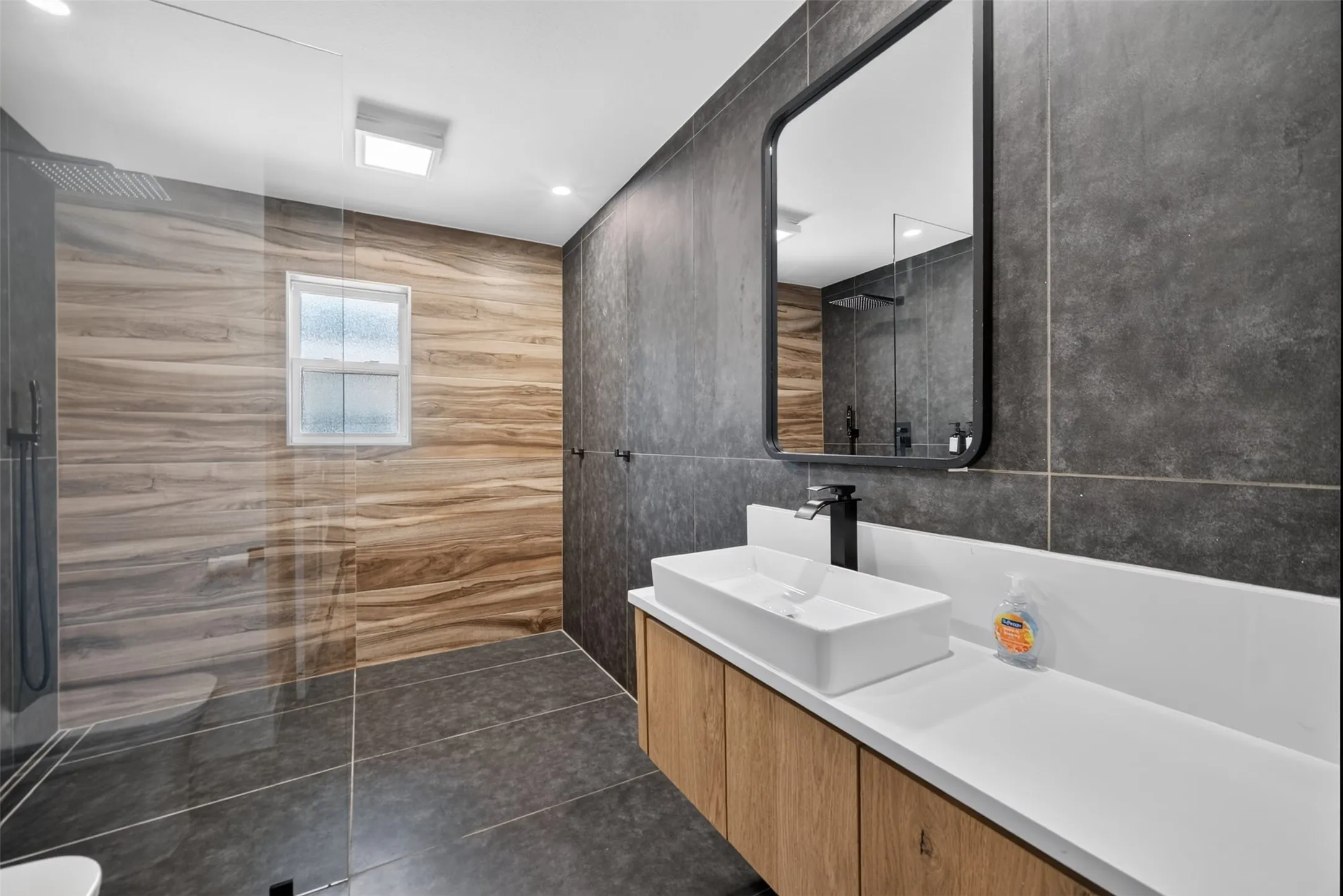 Modern bathroom featuring a wood-finish vanity with a rectangular vessel sink, white countertop, and matte black faucet