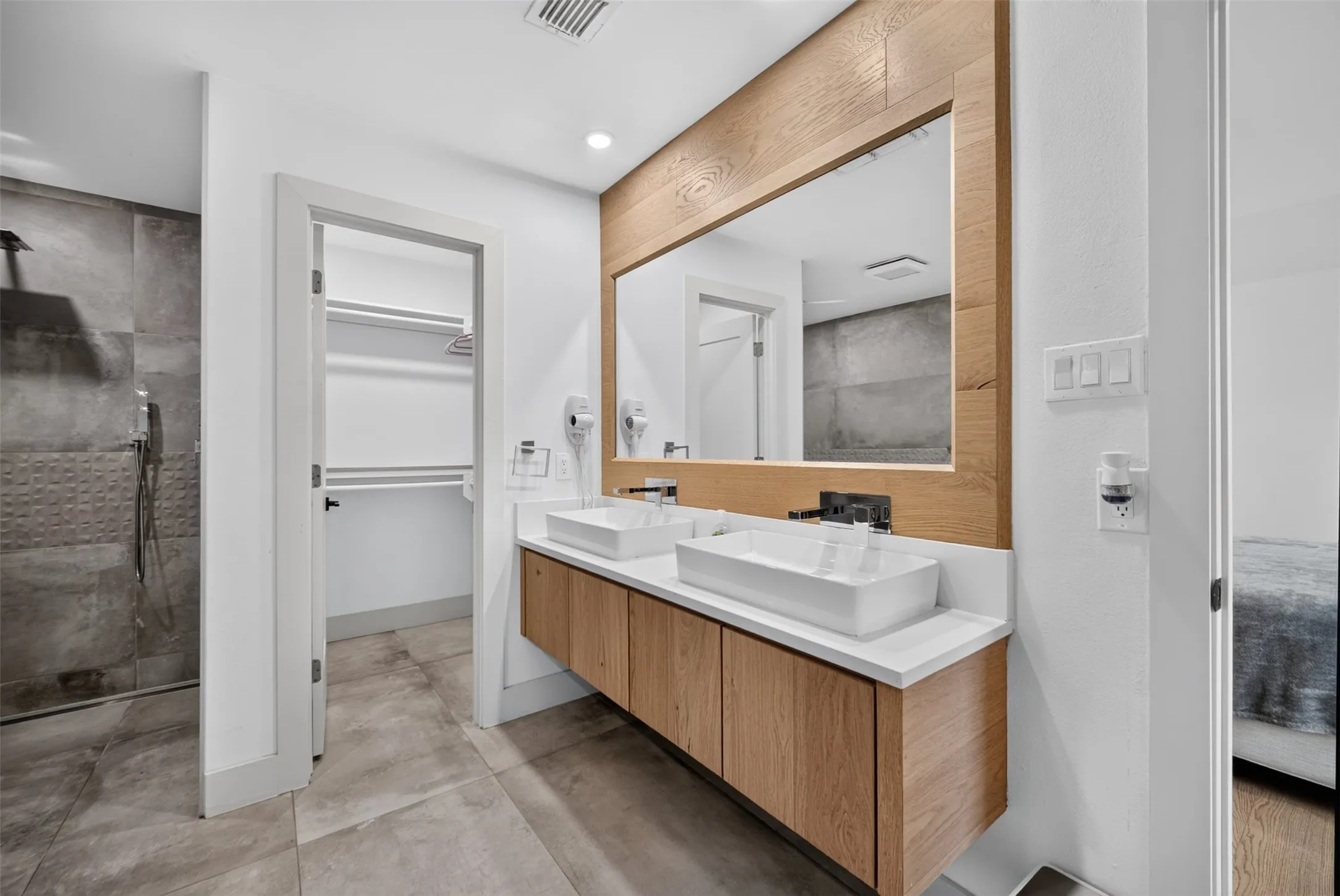 Contemporary bathroom featuring a floating dual vanity with vessel sinks, a large wood-framed mirror, and a walk-in shower with textured tile accents