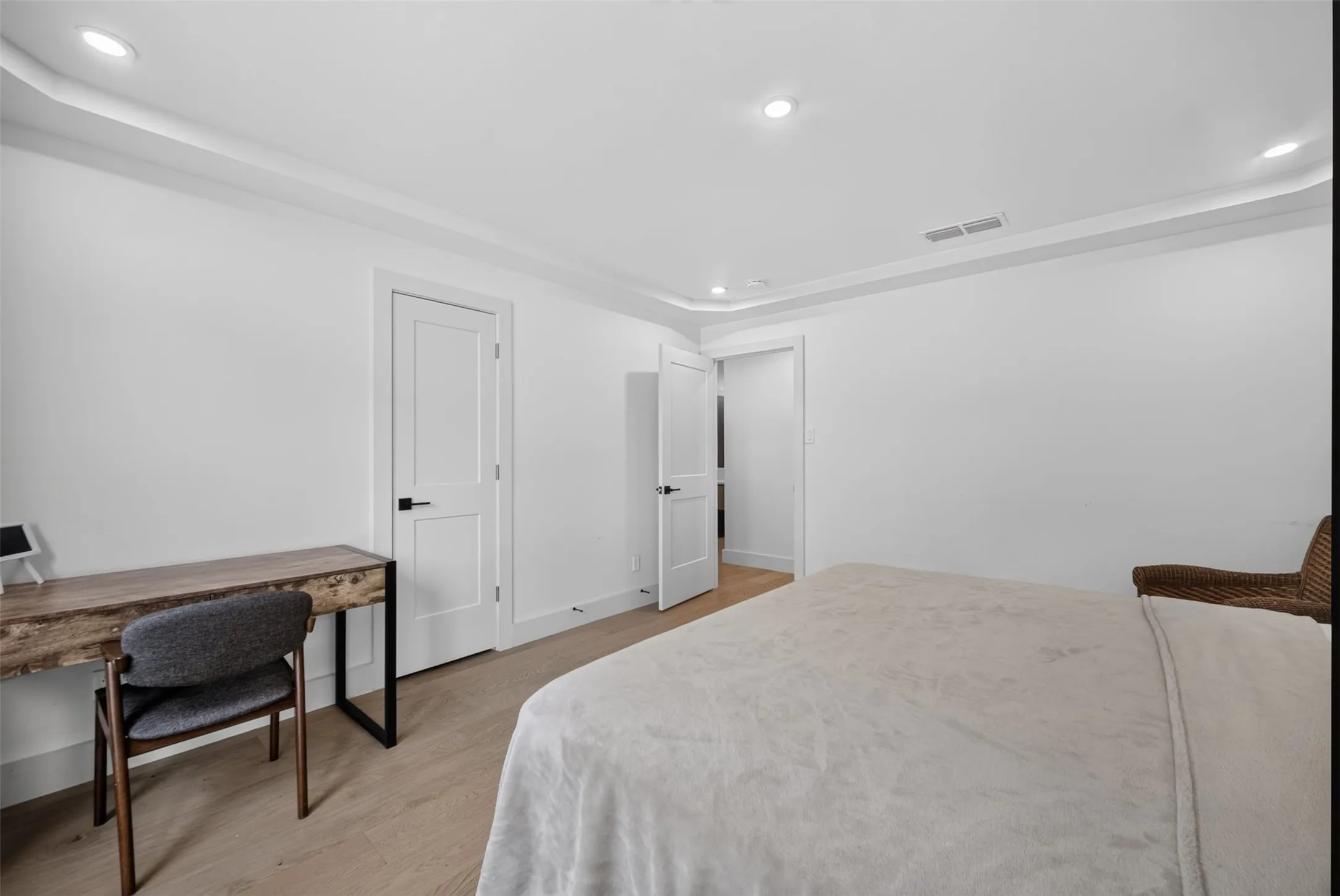 Recessed lighting illuminates a neutral interior featuring wood-finish flooring, white walls, and crown molding