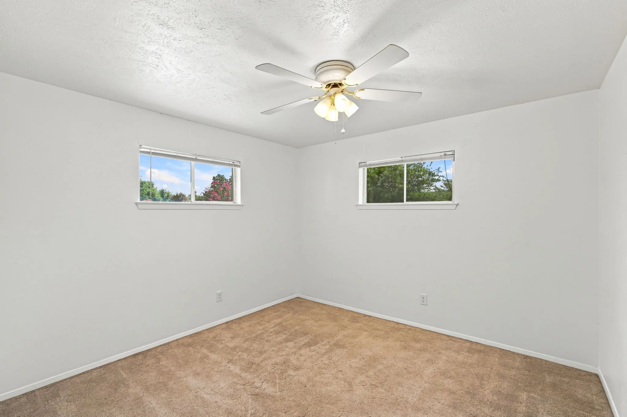 Room featuring neutral carpeting, white walls, two windows with white trim, and a ceiling fan with integrated lighting