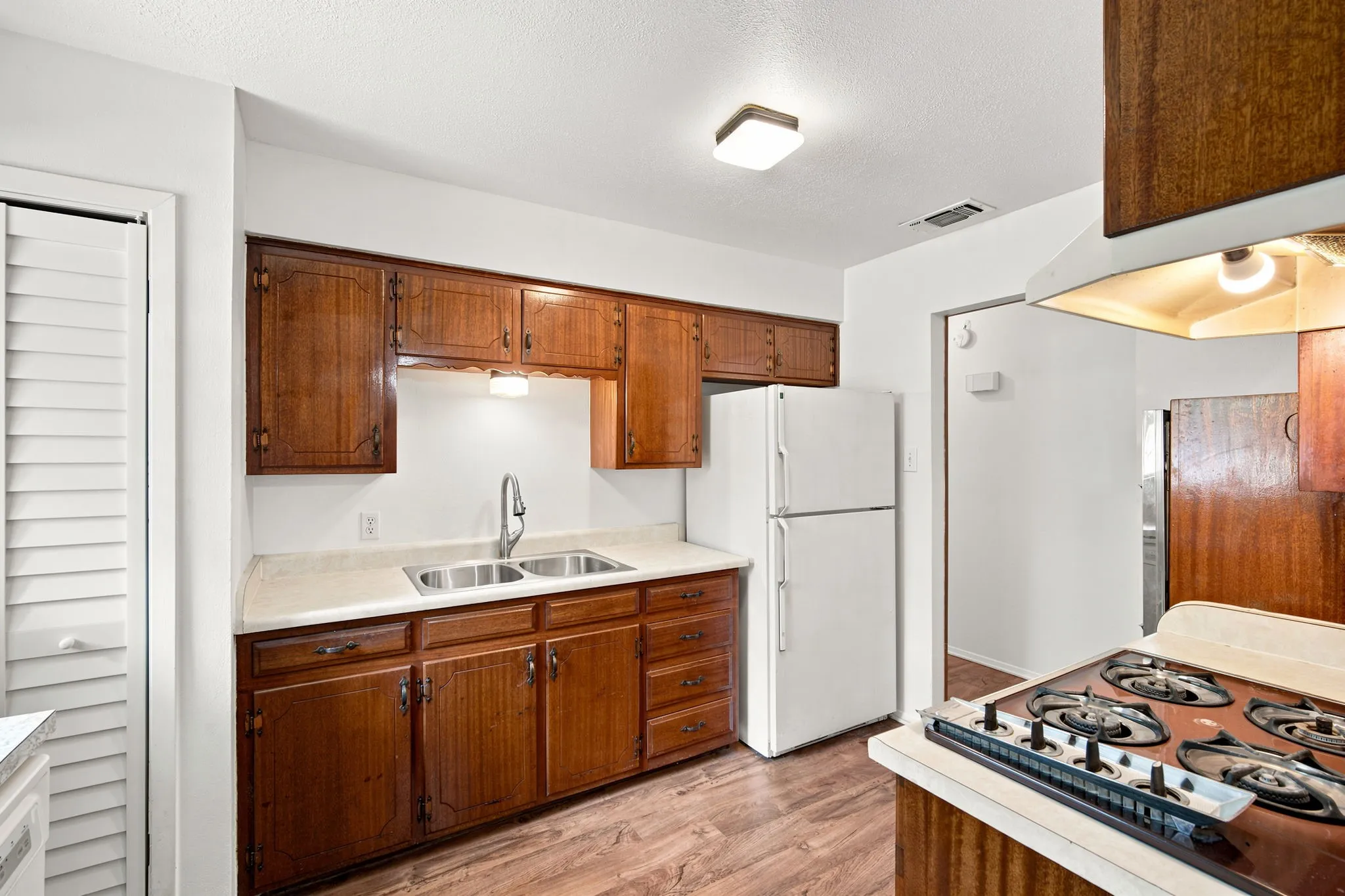 Kitchen featuring wood-finish flooring, wood cabinetry with upper and lower storage, a double basin stainless steel sink, and light-colored countertops