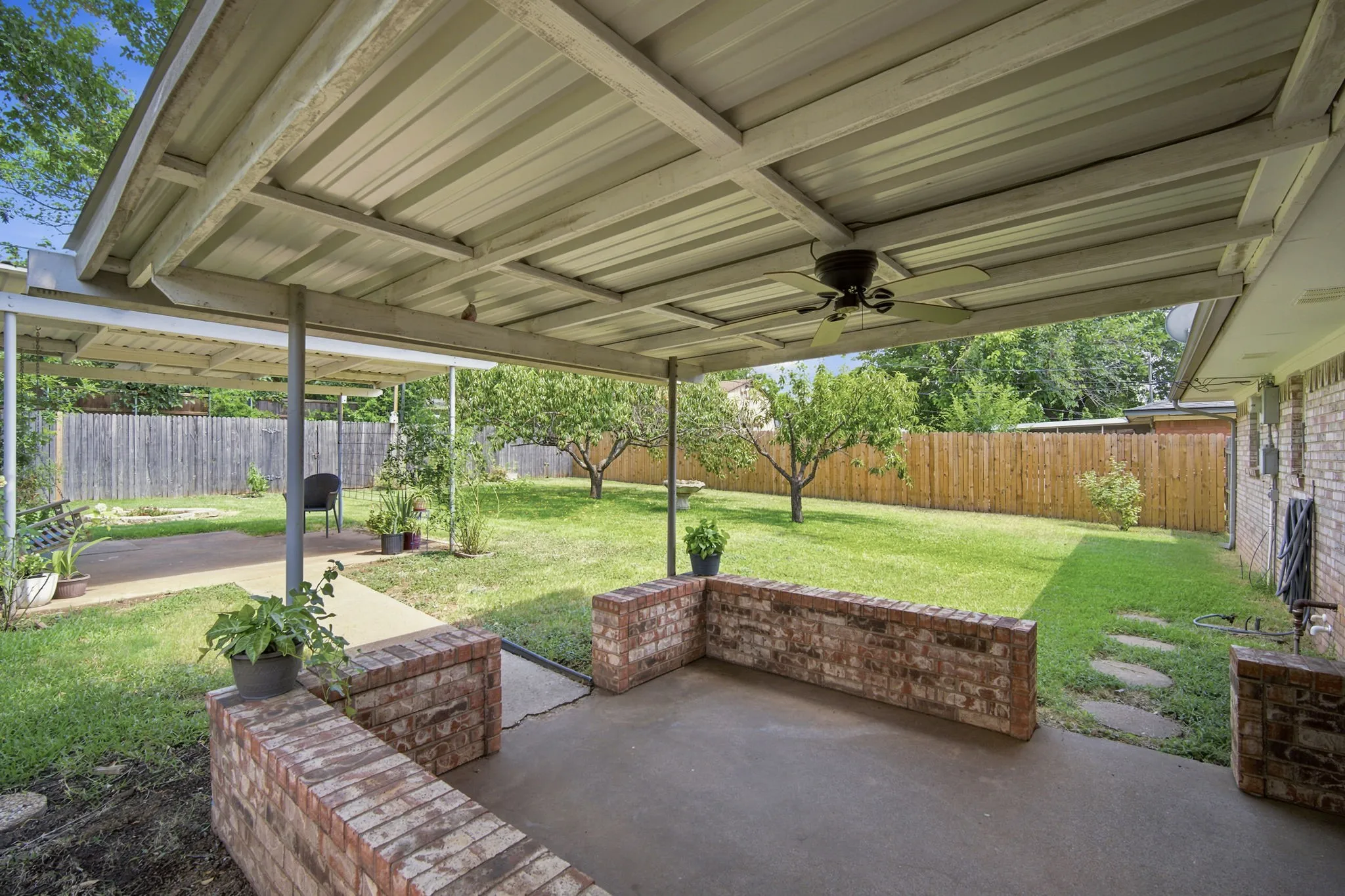 Covered patio featuring a ceiling fan, concrete flooring, and brick half-walls