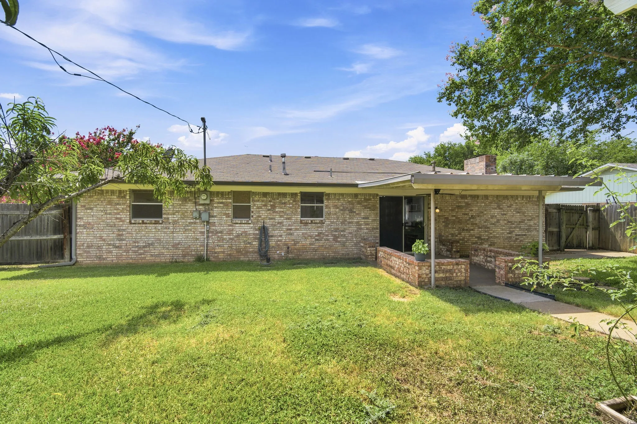 Expansive backyard featuring a brick exterior, covered patio, and mature peach trees