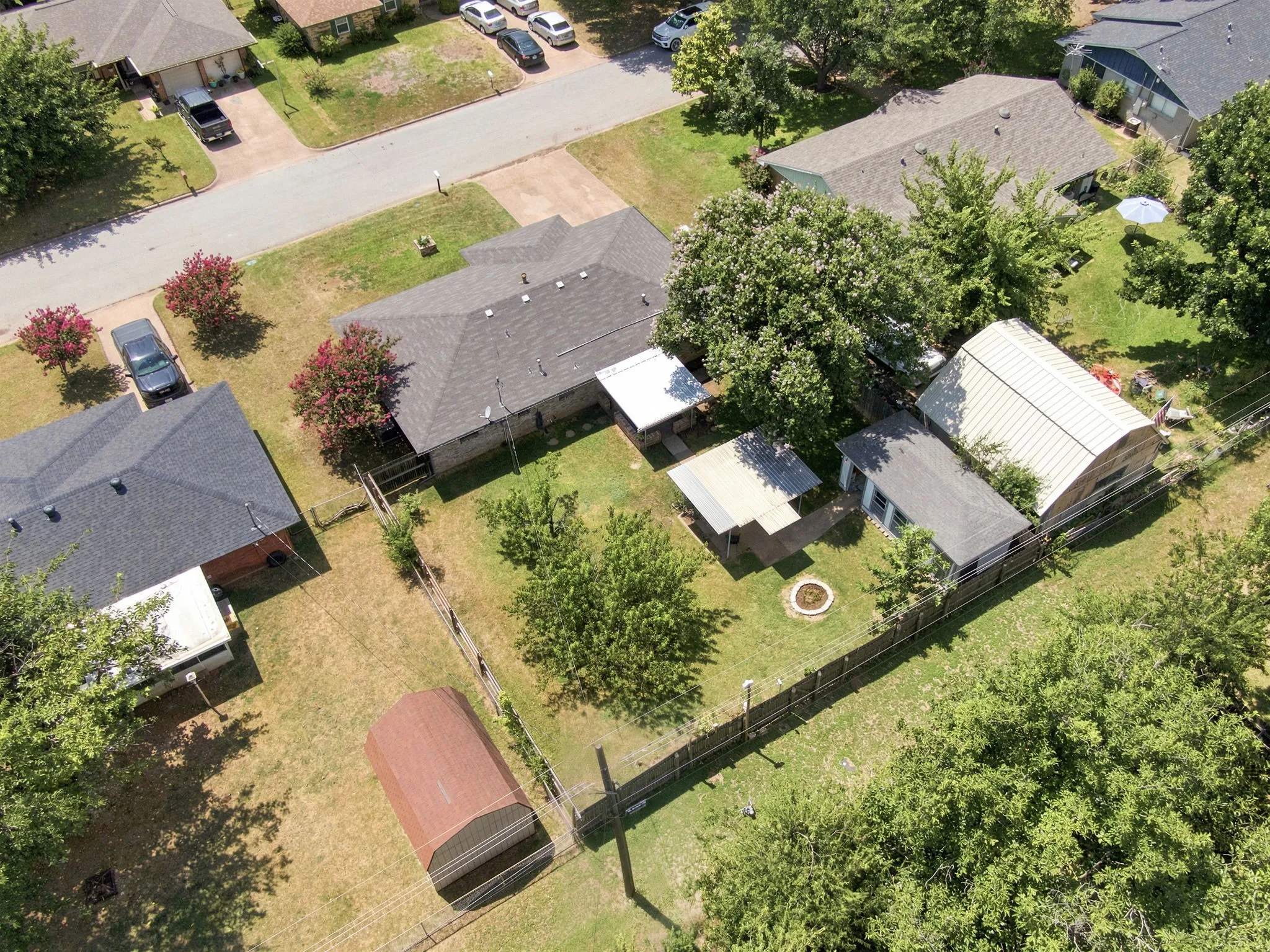 Expansive fenced backyard featuring mature trees, a fire pit, and a outbuilding