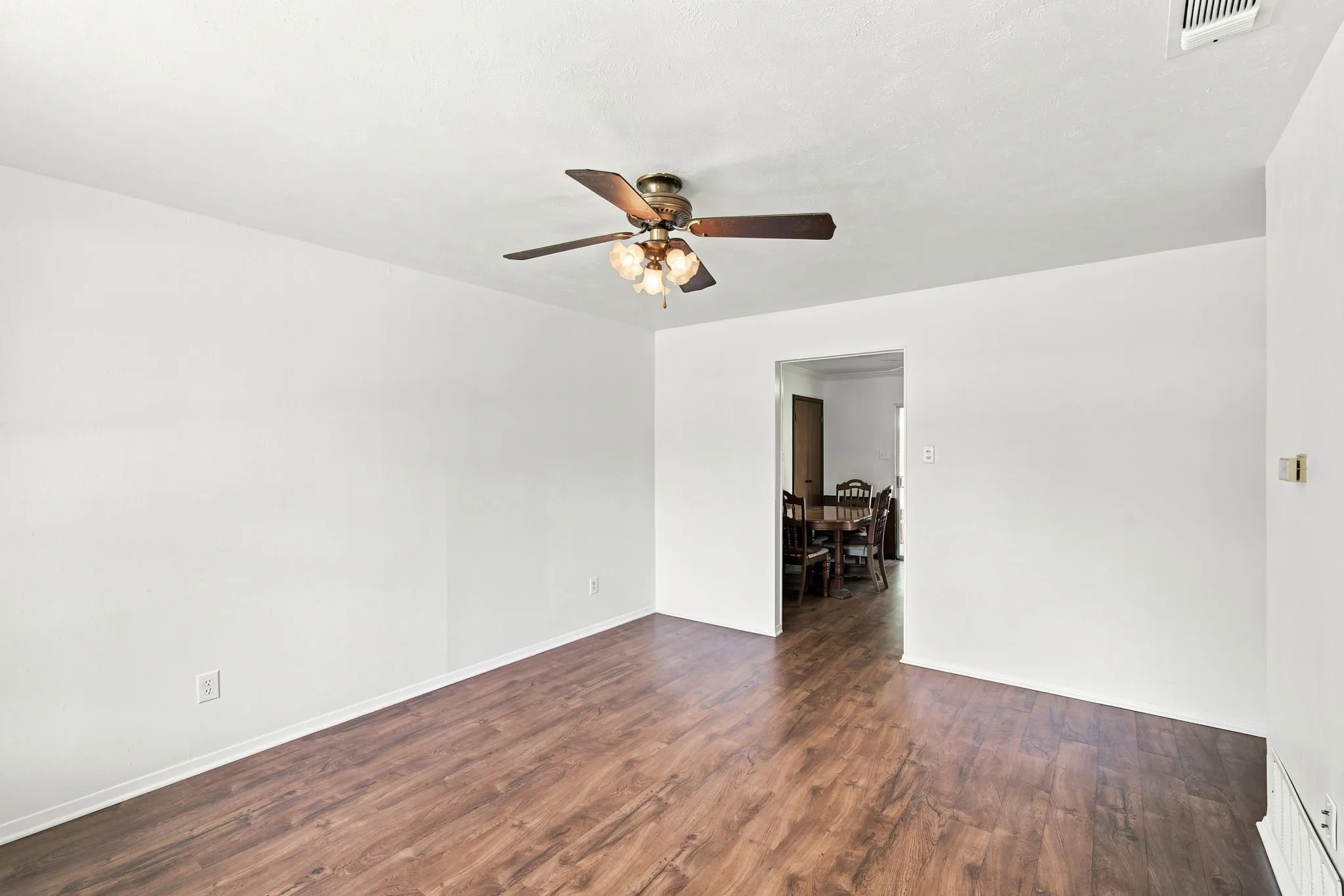 Spacious room featuring wood-finish flooring, crisp white walls, and a ceiling fan with integrated lighting
