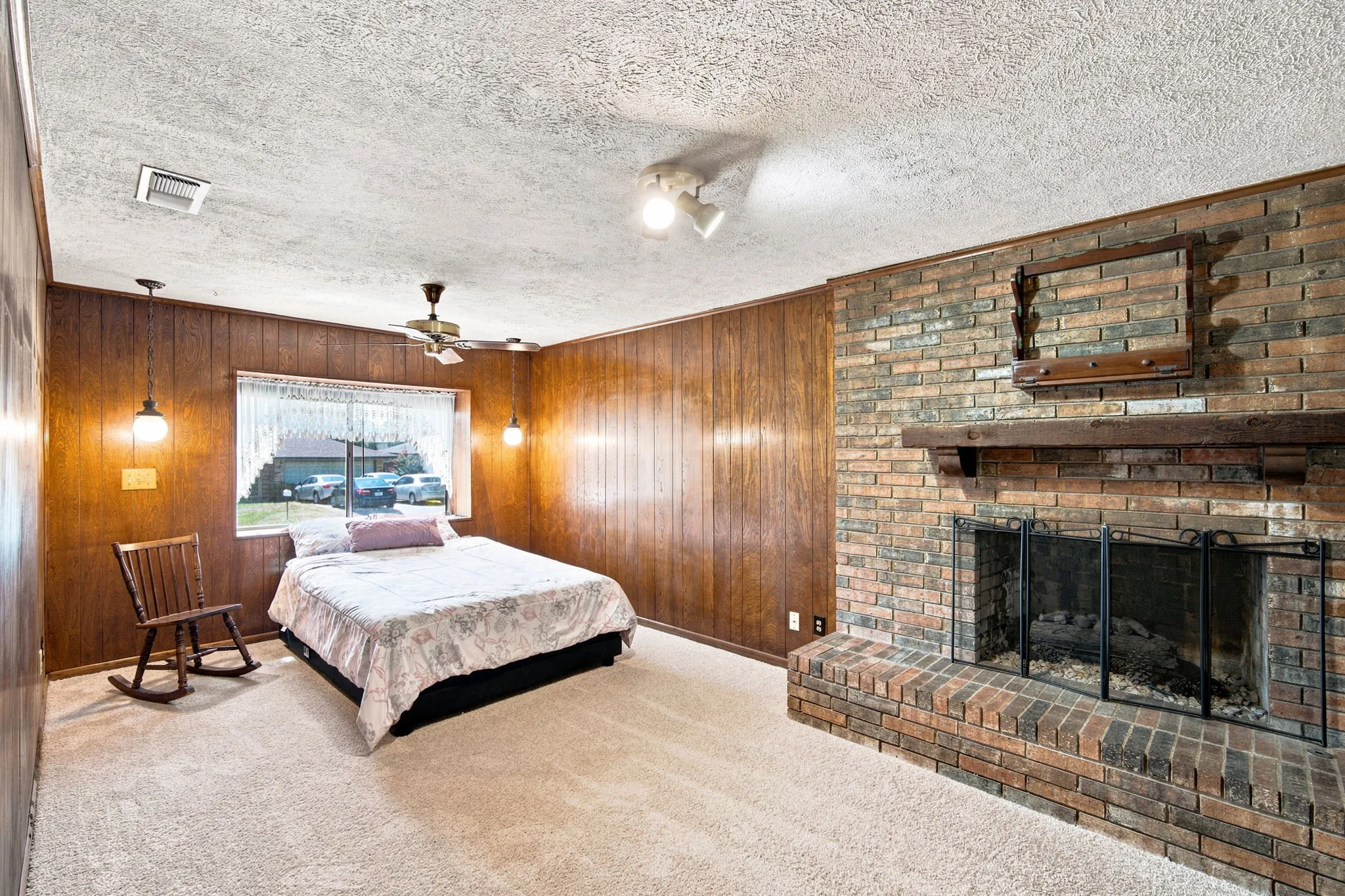 Spacious room featuring a brick fireplace with a wood mantel, wood paneling, and wall-to-wall carpeting