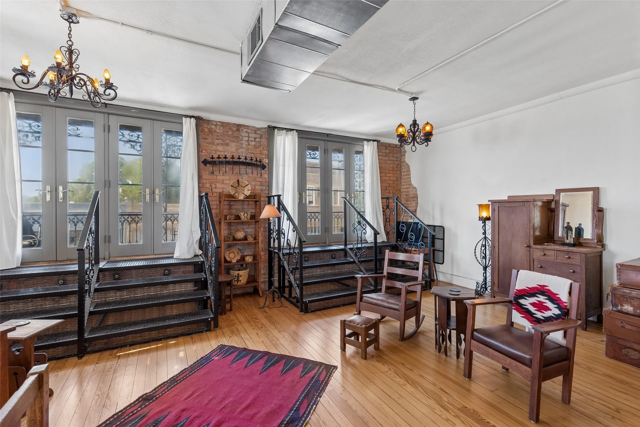 Spacious interior featuring wood-finish flooring, exposed brick accents, and two sets of French doors with wrought iron railings