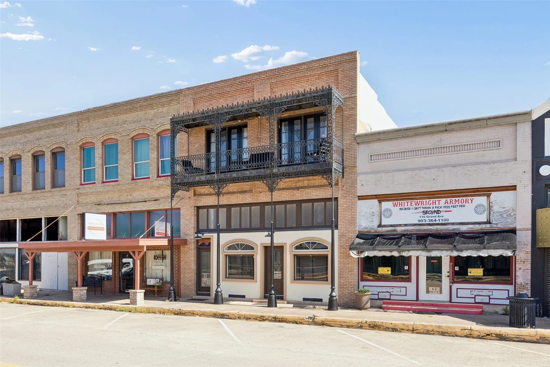 Brick commercial building featuring a second-story wrought iron balcony and full-height windows