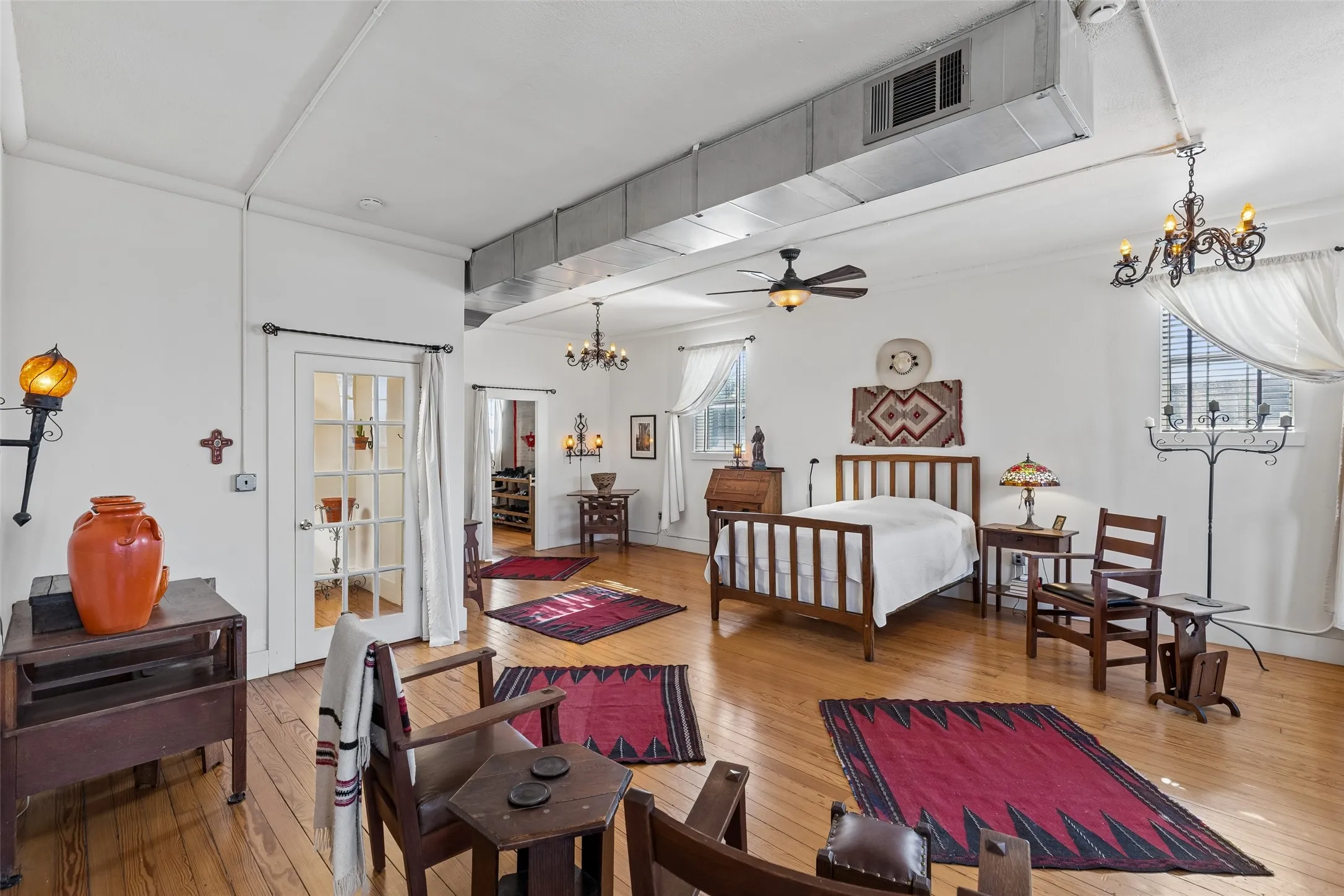 Spacious room featuring hardwood flooring, multiple windows with blinds, exposed ductwork, and white walls