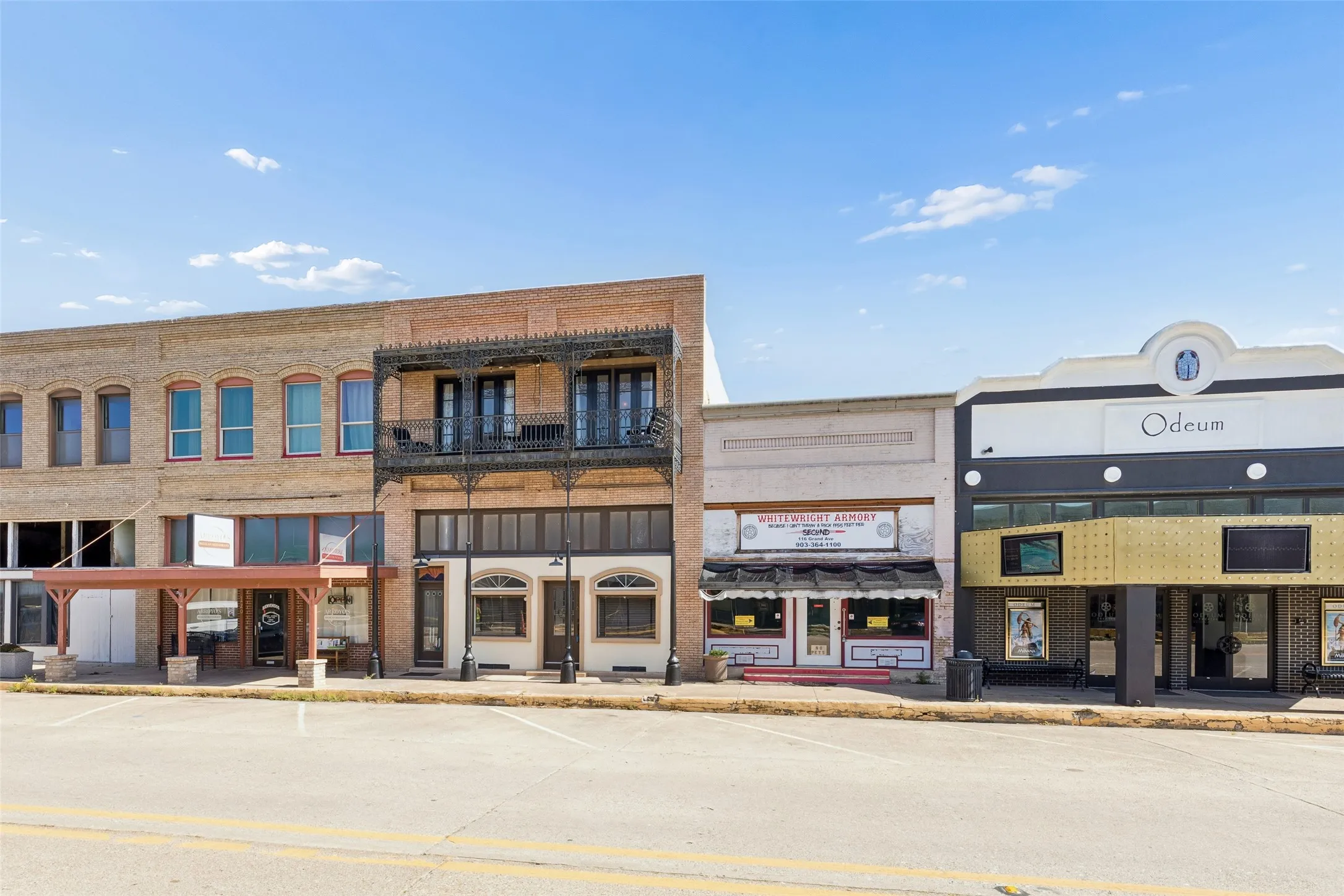 Commercial storefronts featuring brick and stucco facades, street-level display windows, and a prominent second-story balcony with decorative ironwork