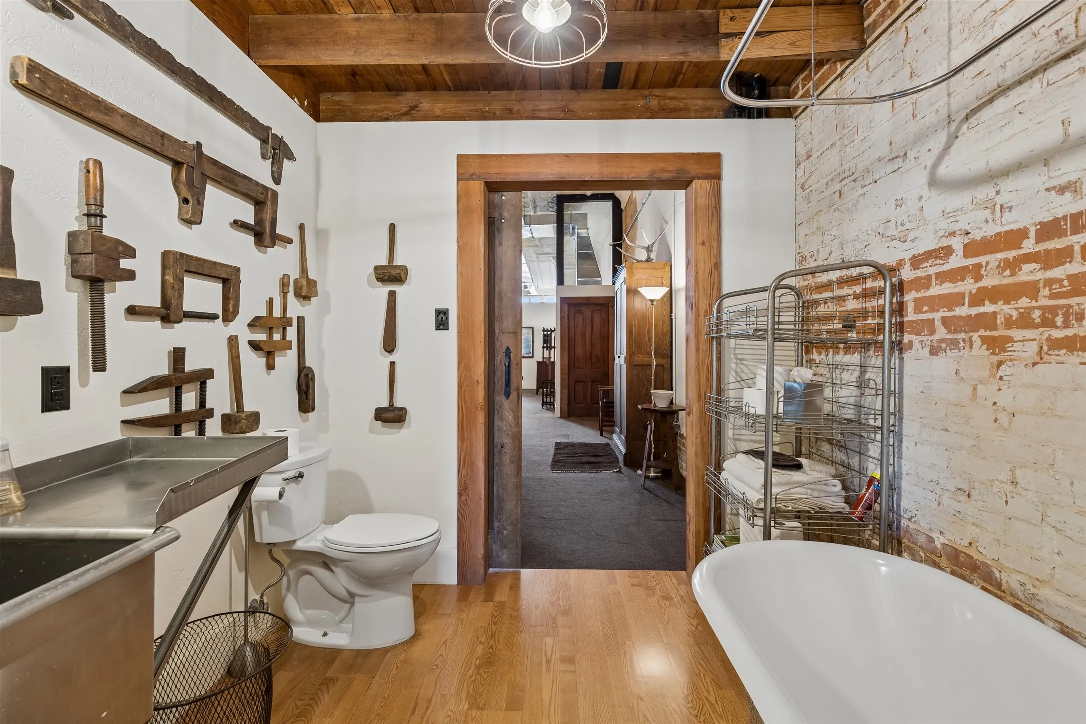Hardwood-finish flooring complementing exposed brick, a freestanding bathtub, and a wood-beamed ceiling