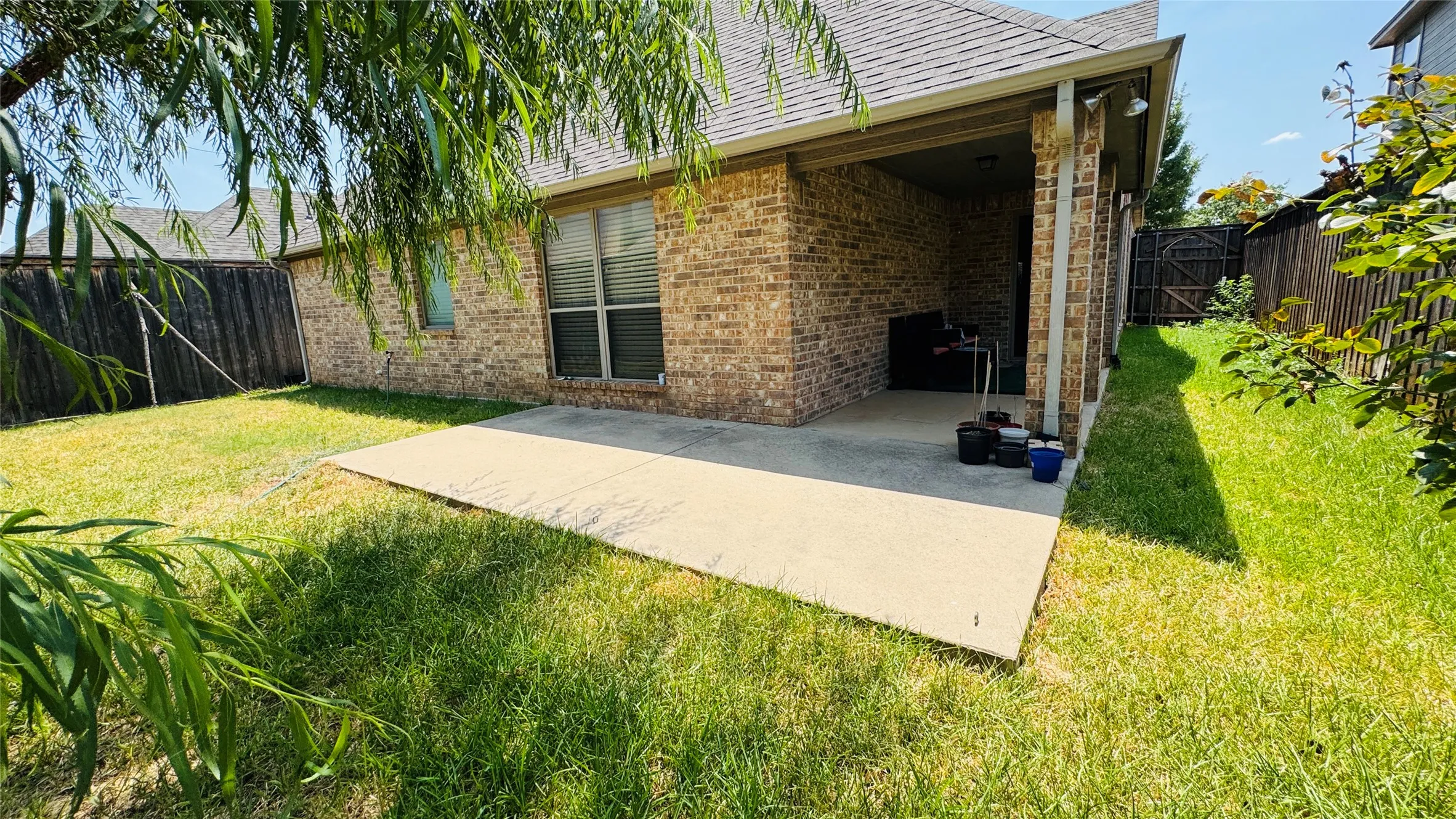Brick exterior with a covered patio, concrete slab, and a fenced backyard