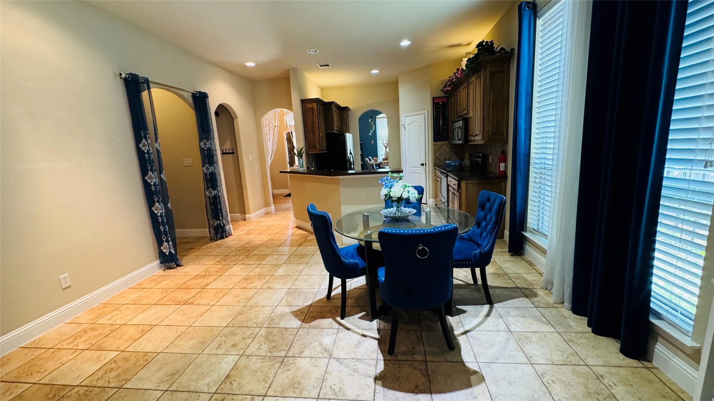 Tiled flooring throughout the dining area and kitchen, featuring arched doorways, recessed lighting, and a kitchen with wood cabinetry and dark countertops