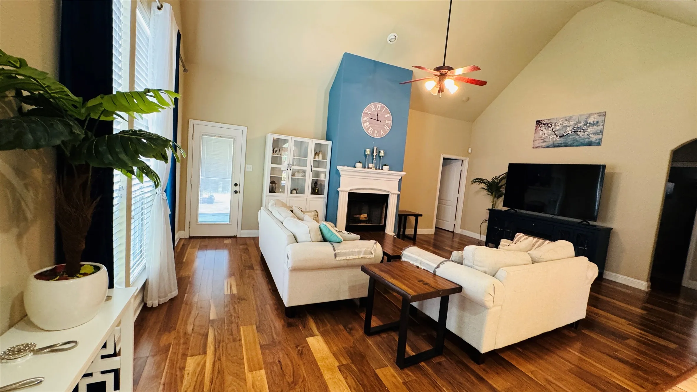 Vaulted ceiling with ceiling fan, wood-finish flooring, built-in fireplace, and a glass-paneled exterior door