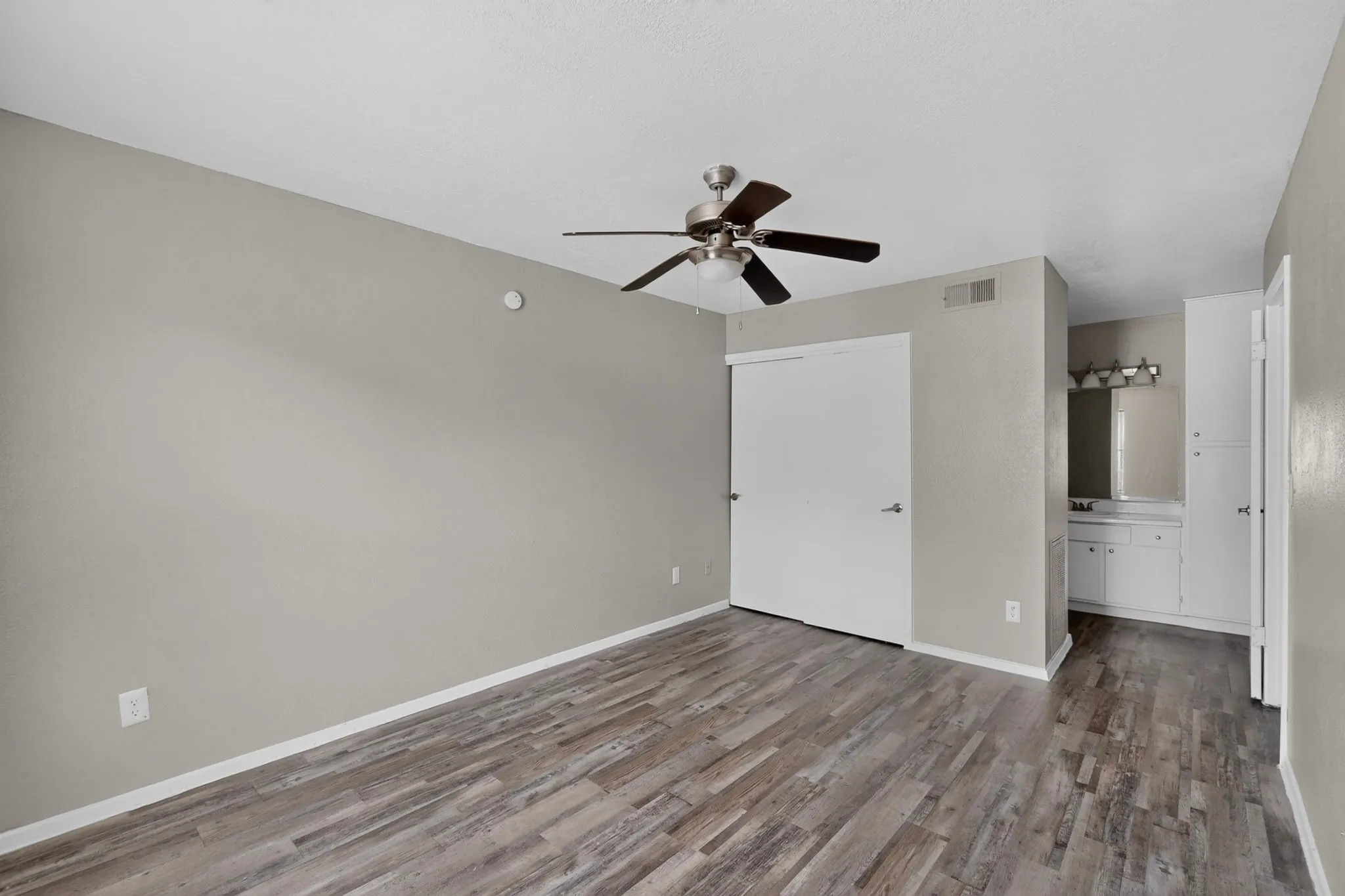 Spacious room featuring wood-finish flooring, a ceiling fan with light fixture, and a neutral wall color