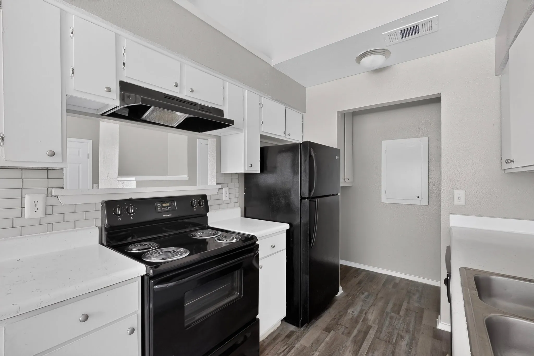 Kitchen featuring white cabinetry, white countertops, a black electric range with an overhead vent, and a black refrigerator