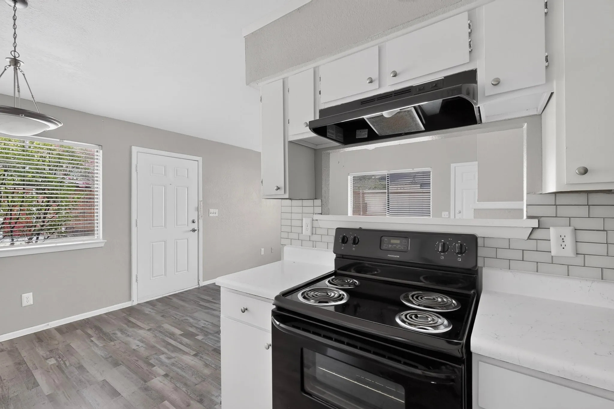 Kitchen area featuring wood-finish flooring, white cabinetry, a black electric range, and a white subway tile backsplash
