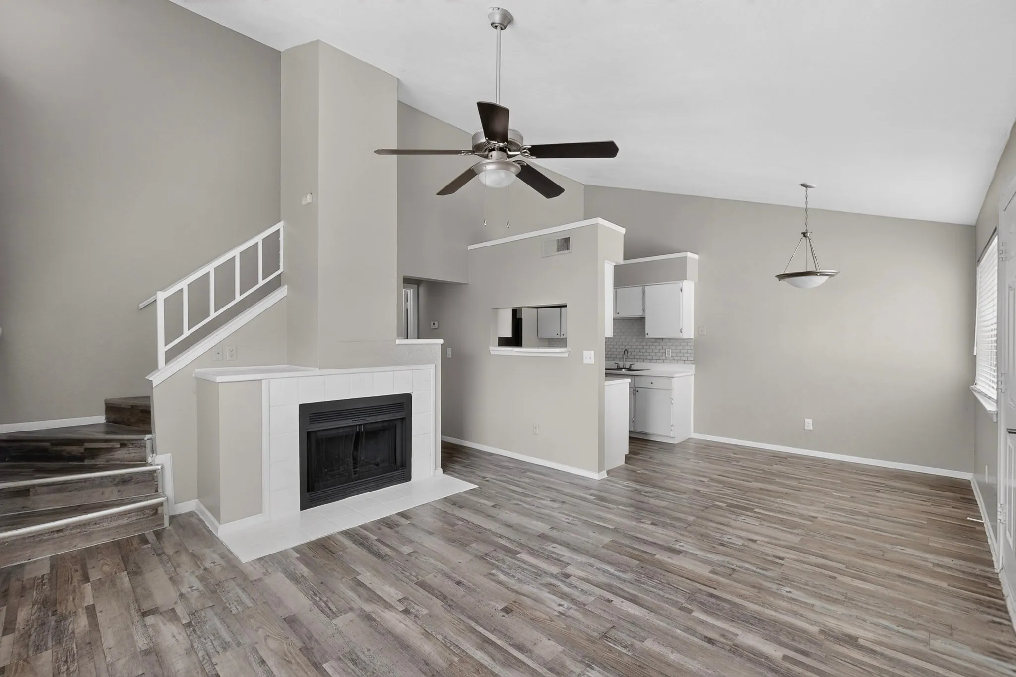 Living area featuring a fireplace with a white mantel, wood-finish flooring, and a vaulted ceiling