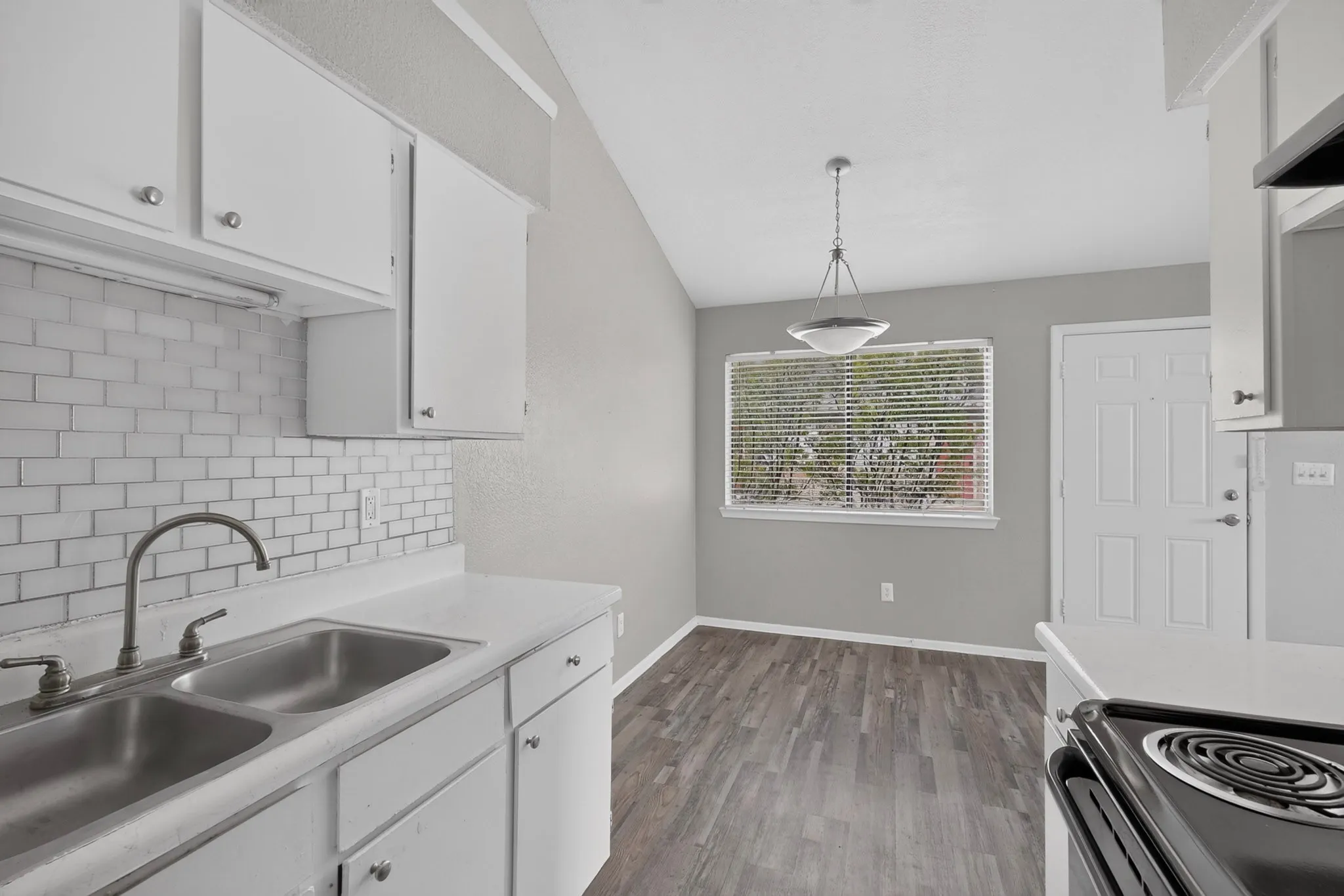 Kitchen featuring white cabinetry with silver hardware, dual basin stainless steel sink, subway tile backsplash, and light-toned countertops
