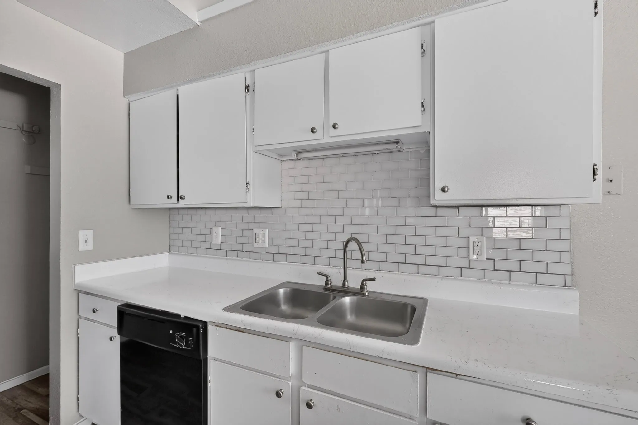Kitchen featuring white cabinetry, white countertops, subway tile backsplash, double basin stainless steel sink, and a black dishwasher