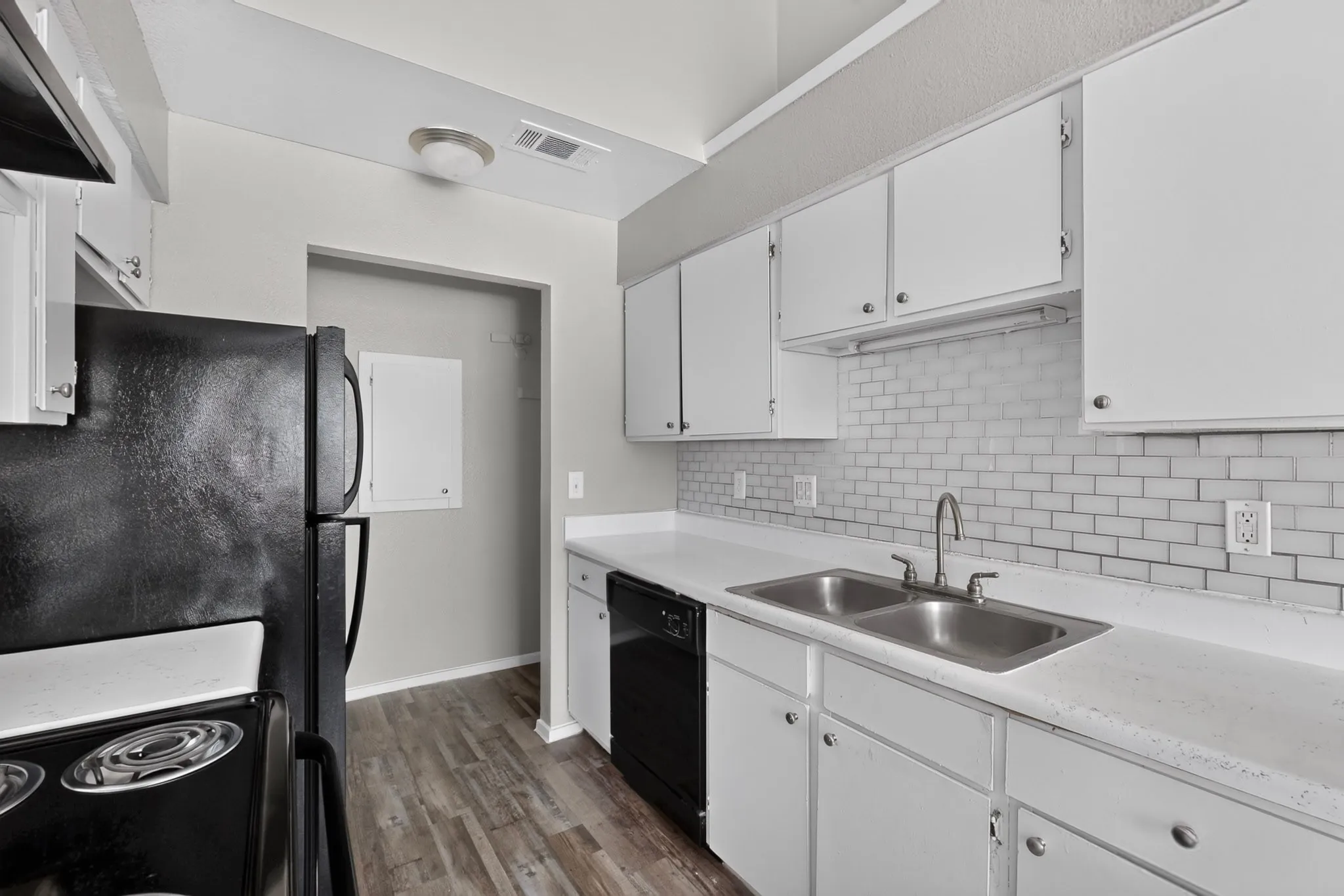 Kitchen featuring white cabinetry, white countertops, a stainless steel double sink, a subway tile backsplash, and wood-finish flooring
