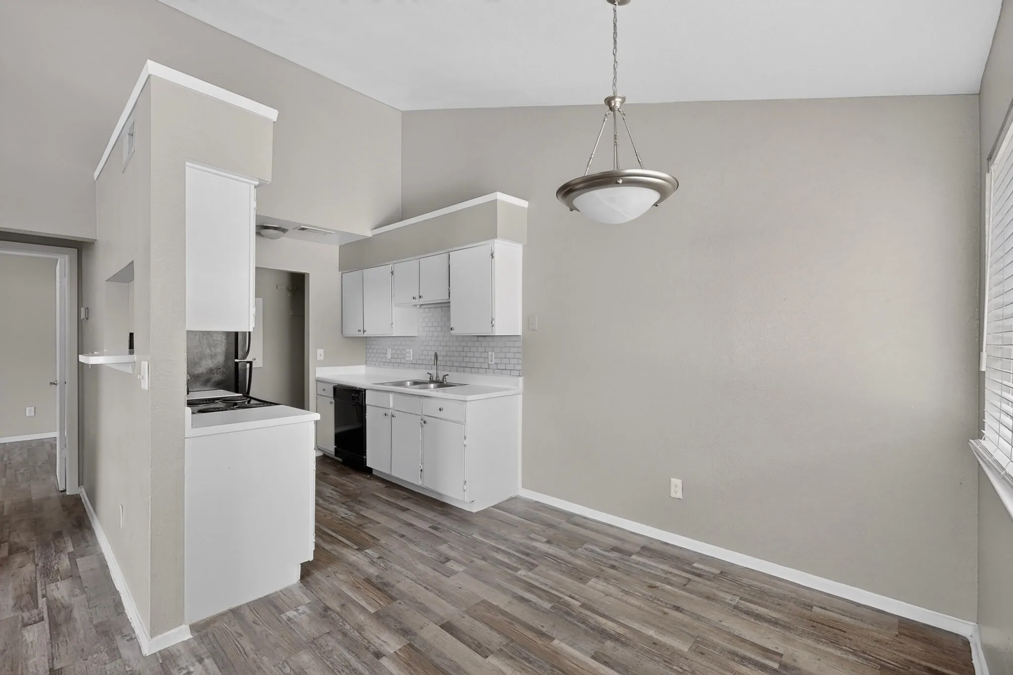 Kitchen and dining area featuring vaulted ceilings, wood-finish flooring, white cabinetry, a subway tile backsplash, and a built-in black dishwasher