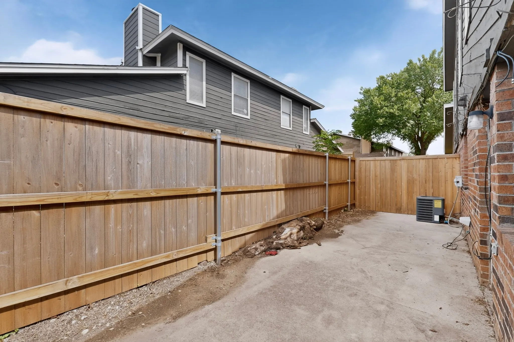 Exterior concrete patio area featuring a privacy fence, brick wall, and siding