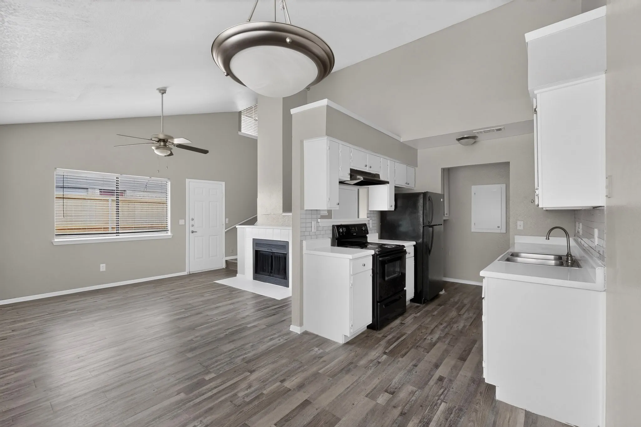 Open-concept living space featuring vaulted ceilings, wood-finish flooring, and a fireplace with a tile surround