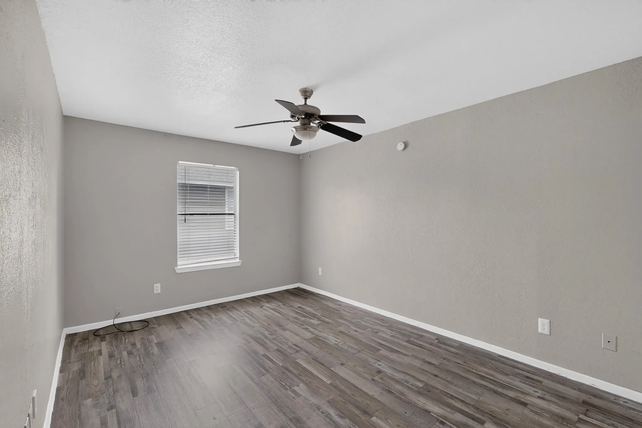 Spacious room featuring wood-finish flooring, a window with horizontal blinds, and a ceiling fan with integrated lighting