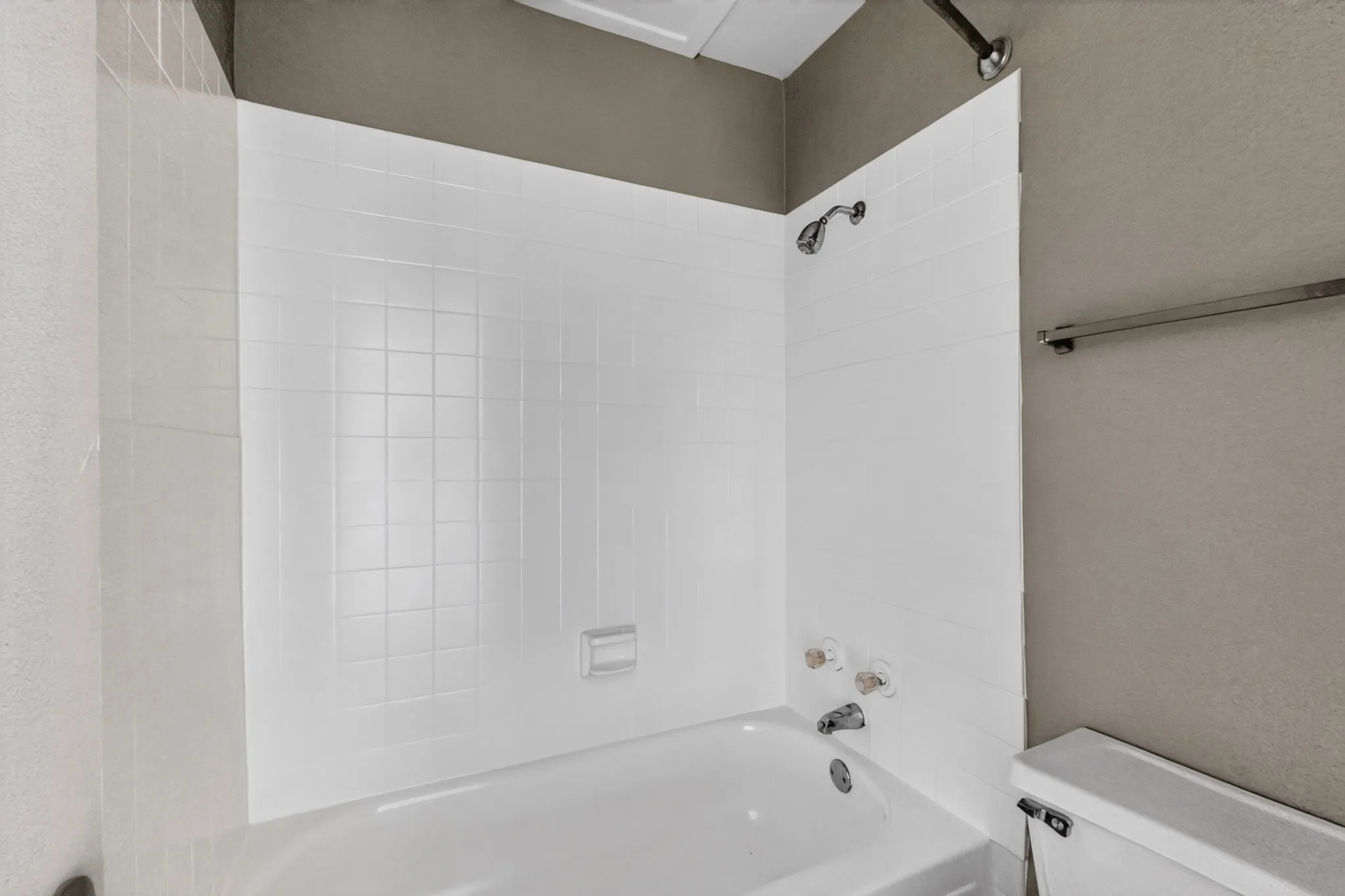 Bathtub and shower combination featuring white tiled surround, chrome fixtures, and a neutral wall color