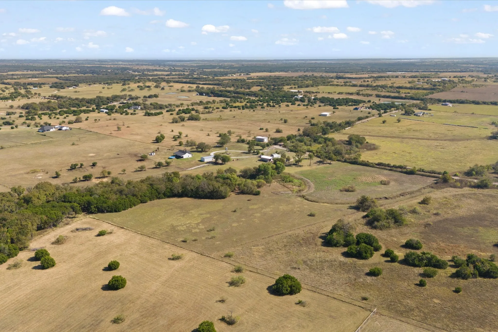 Expansive rural landscape featuring scattered residential structures, mature tree lines, and open fields with varying vegetation