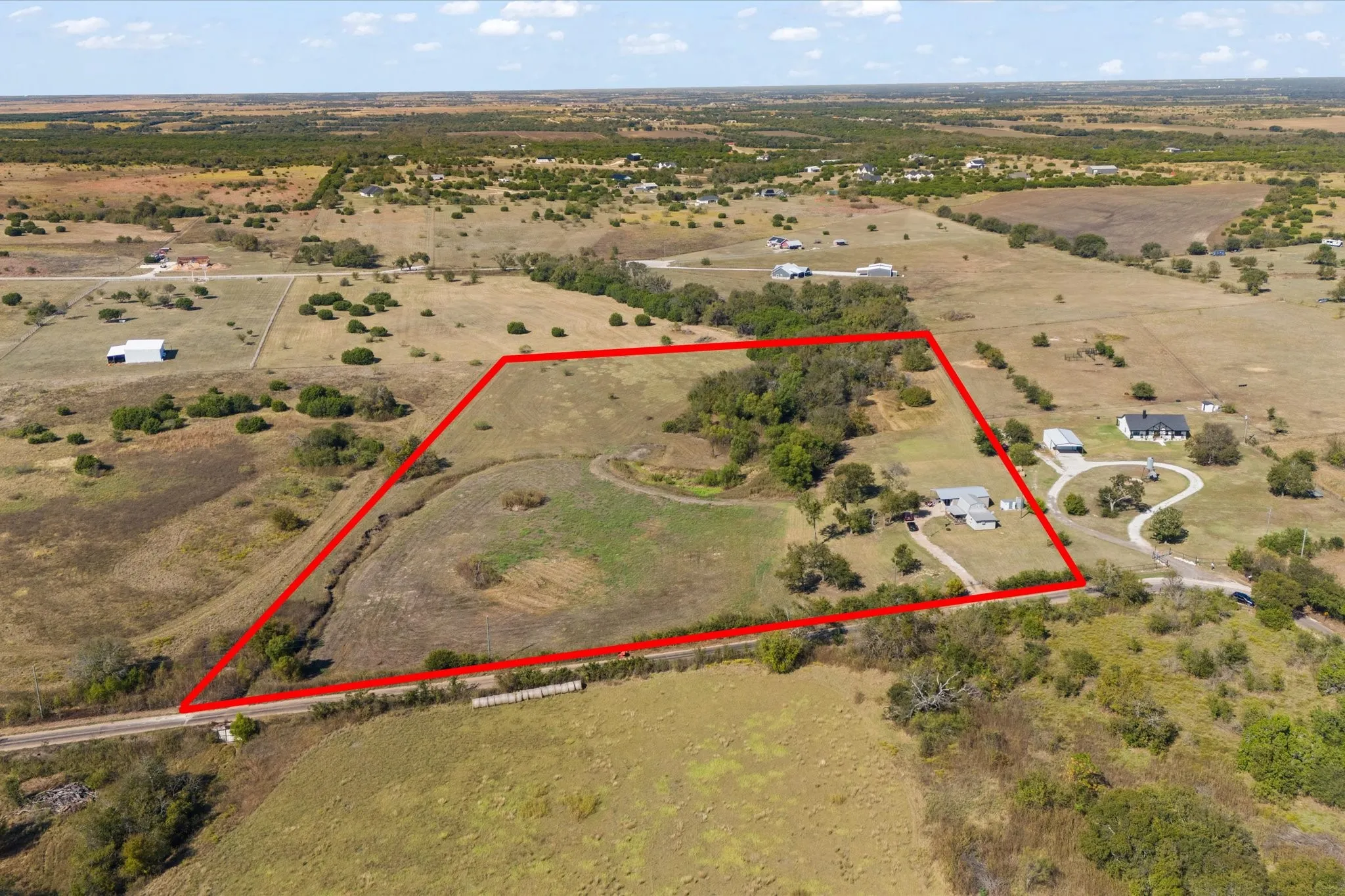Expansive undeveloped land featuring a cleared building site, mature trees, and a paved road frontage