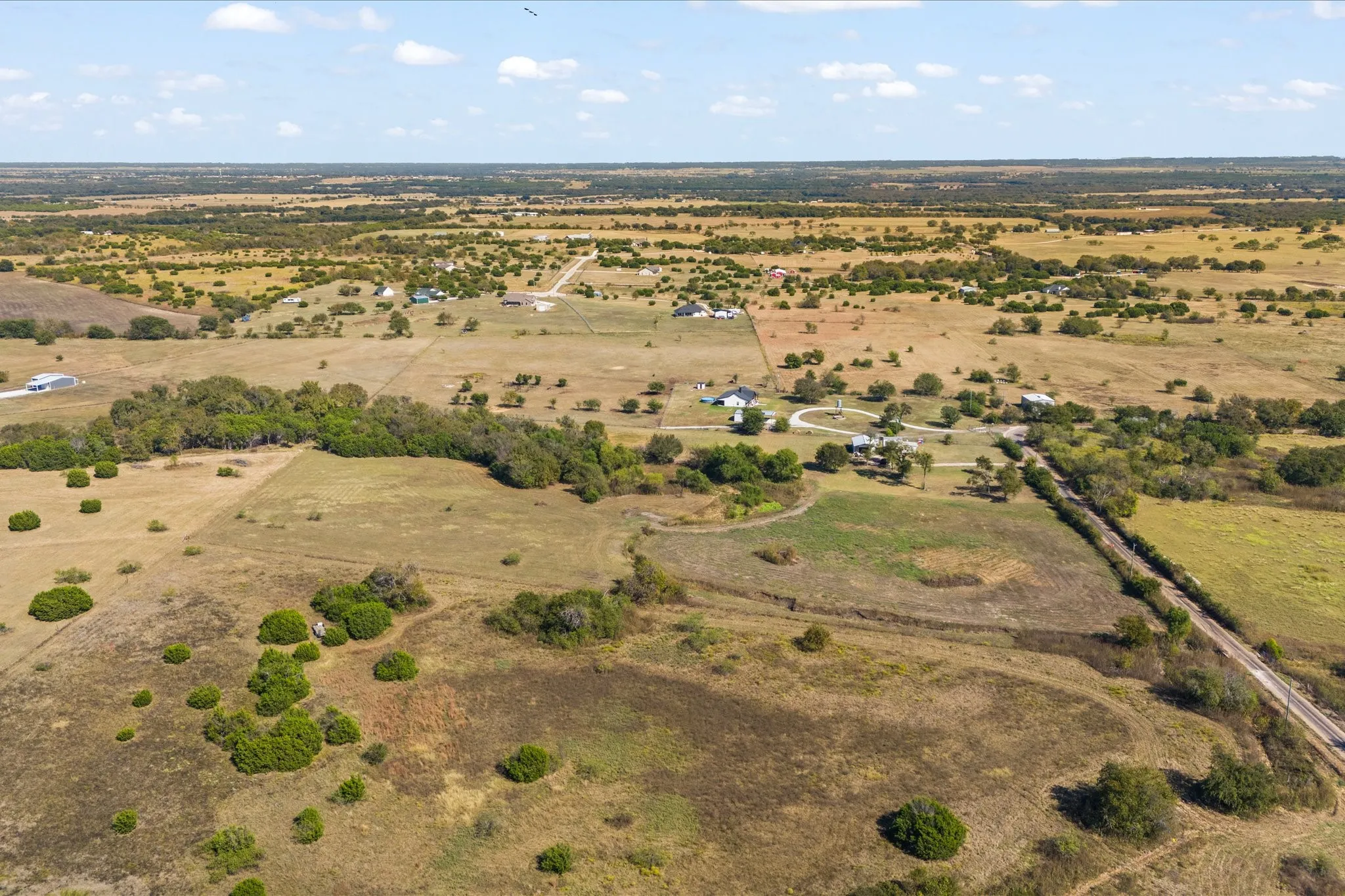 Expansive rural landscape featuring scattered trees, open fields, and distant residential structures