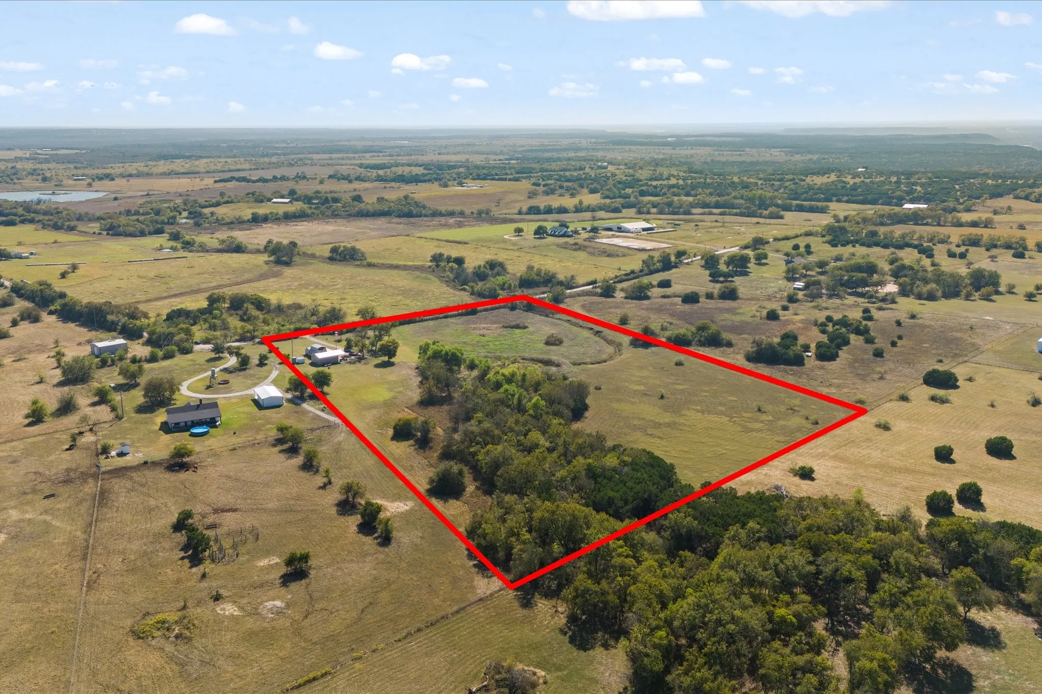 Expansive rural property featuring an open field, scattered trees, and distant water bodies