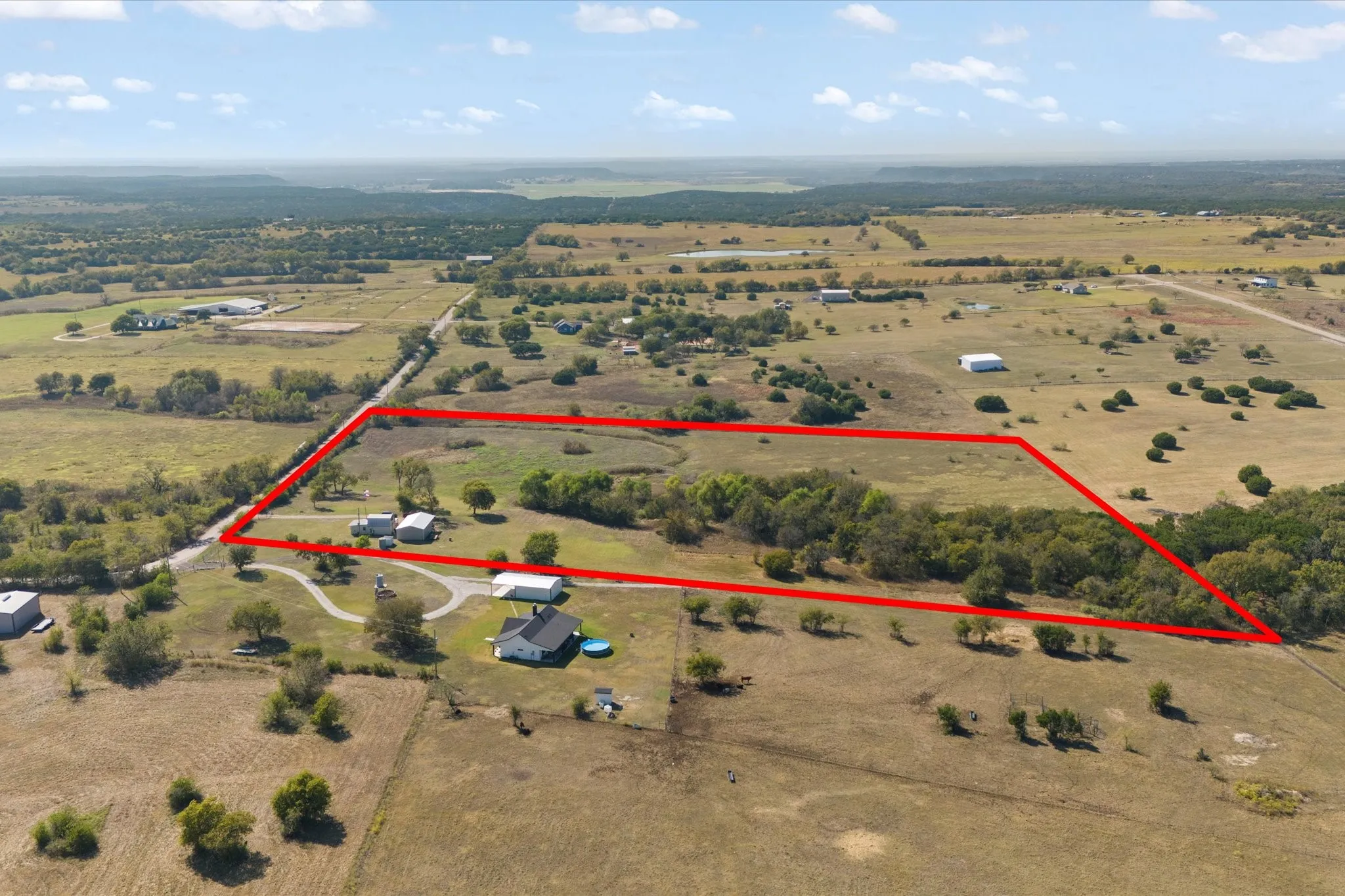 Expansive rural property featuring a defined perimeter, multiple structures, and a winding driveway