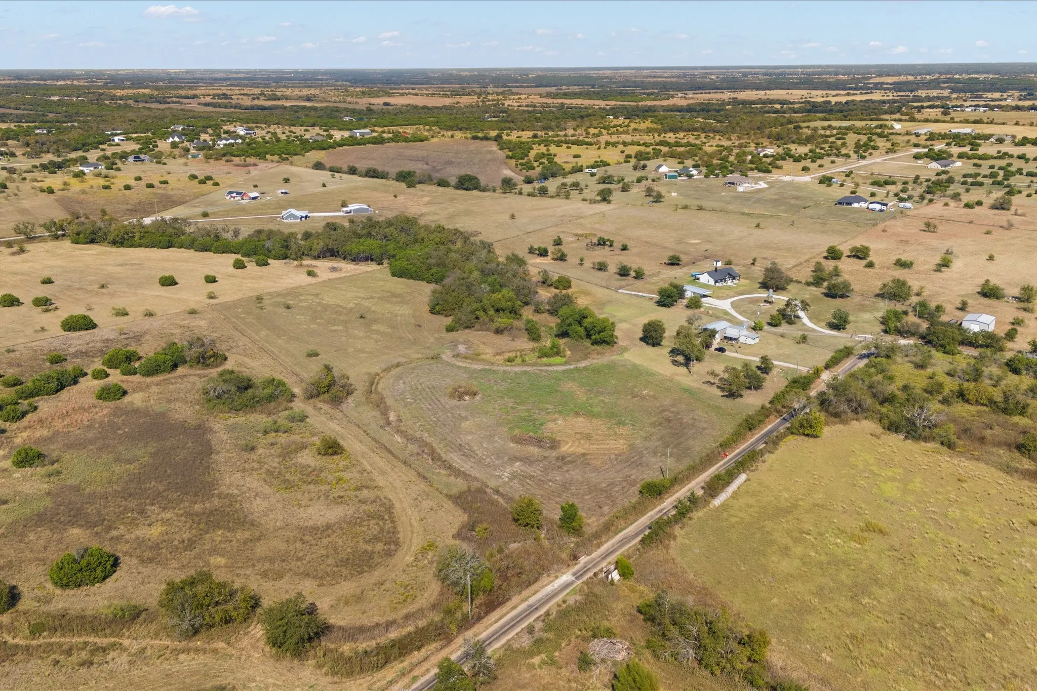 Expansive rural landscape featuring scattered residential properties, mature trees, and open fields under a clear sky