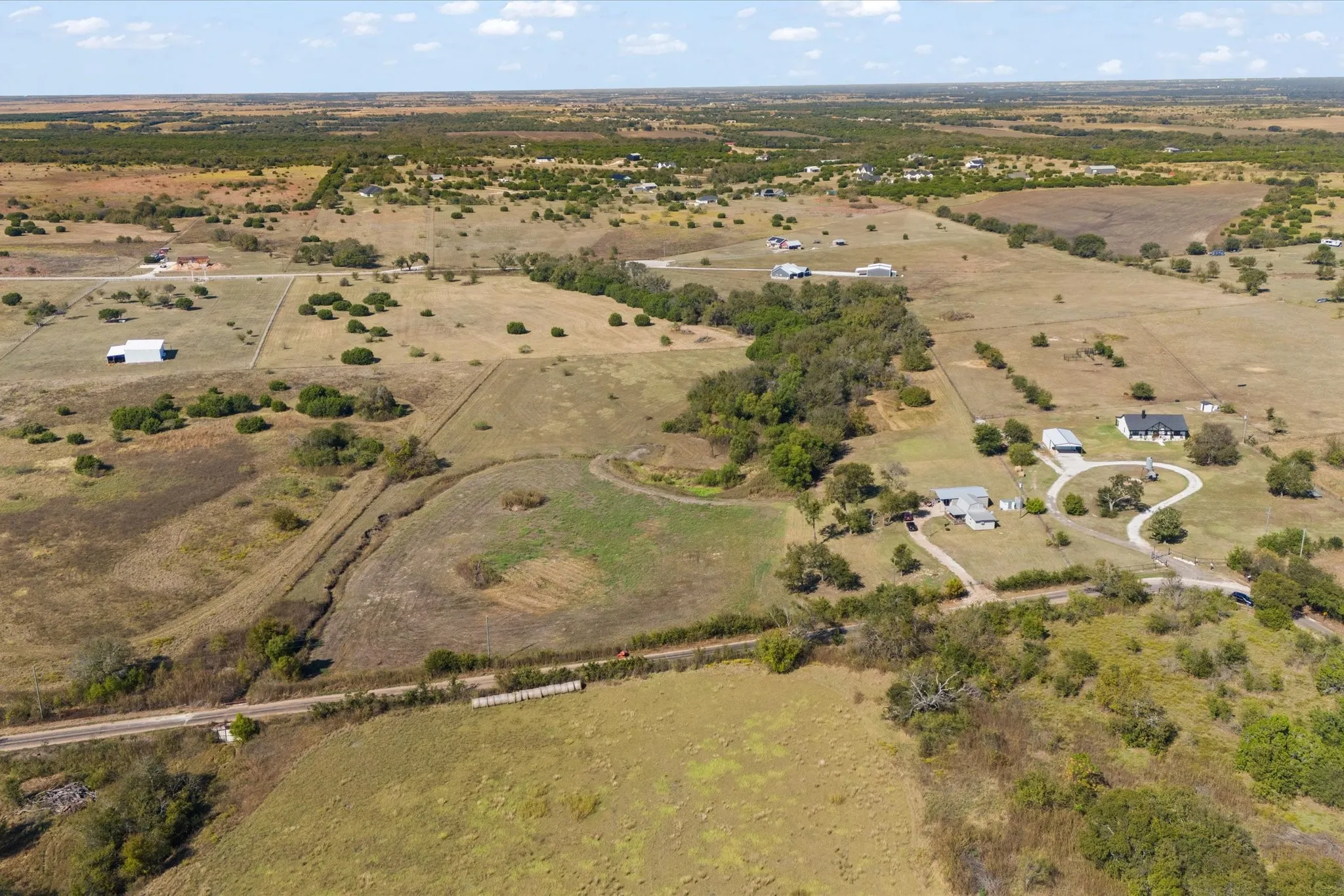 Expansive rural landscape featuring multiple structures, open fields, scattered trees, and winding driveways