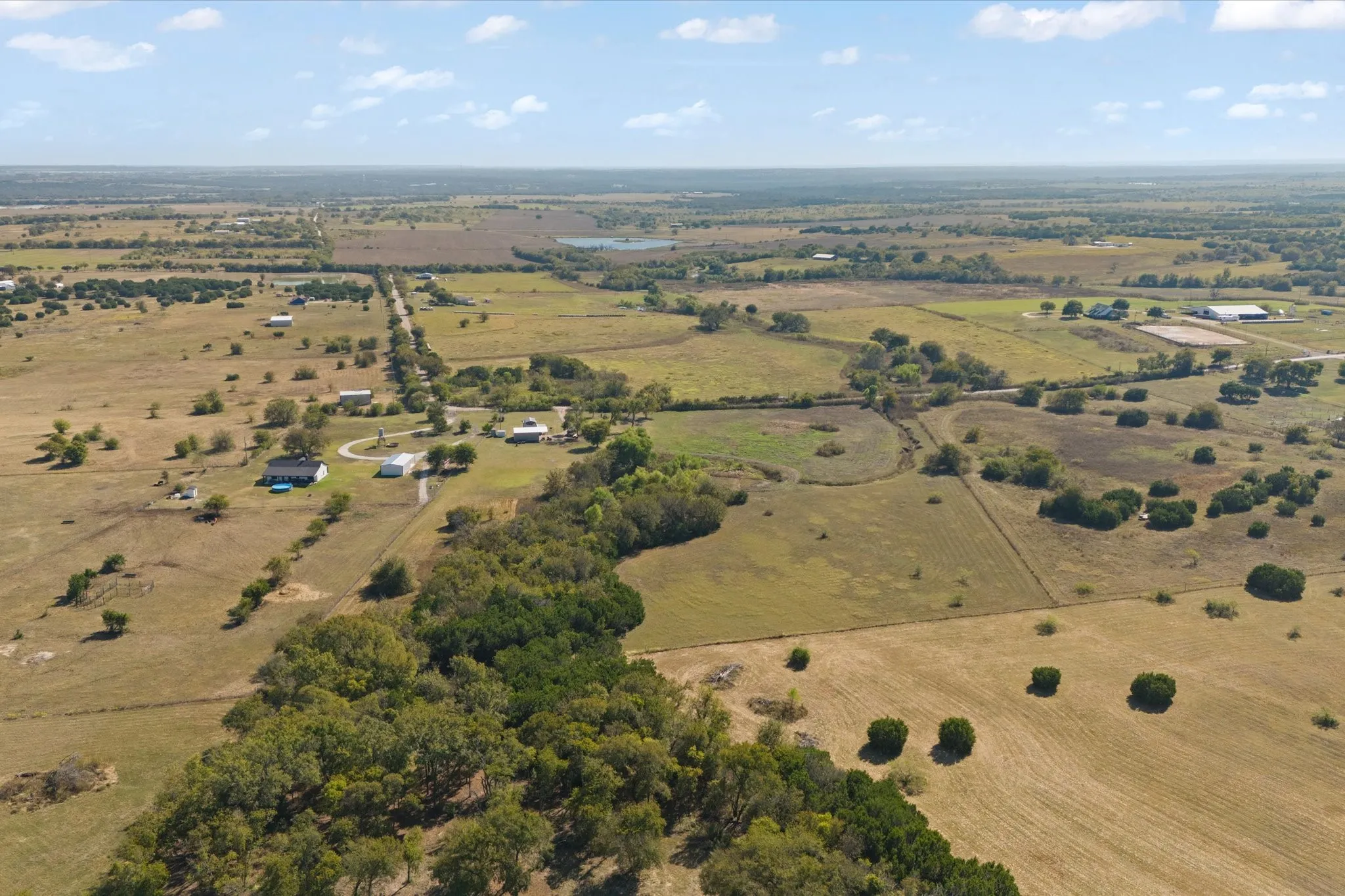 Expansive rural landscape featuring scattered homes, mature trees, open fields, and a prominent pond