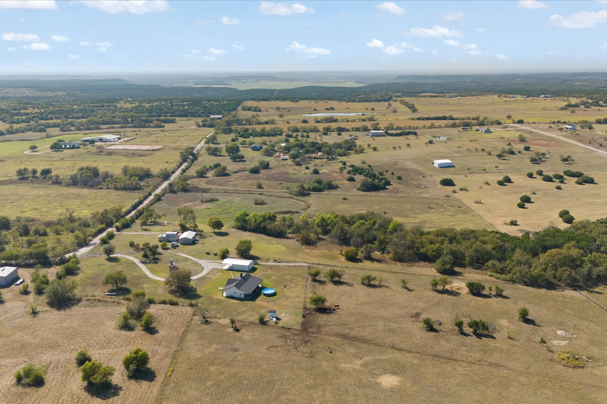 Aerial perspective showcasing extensive acreage with scattered trees and multiple structures
