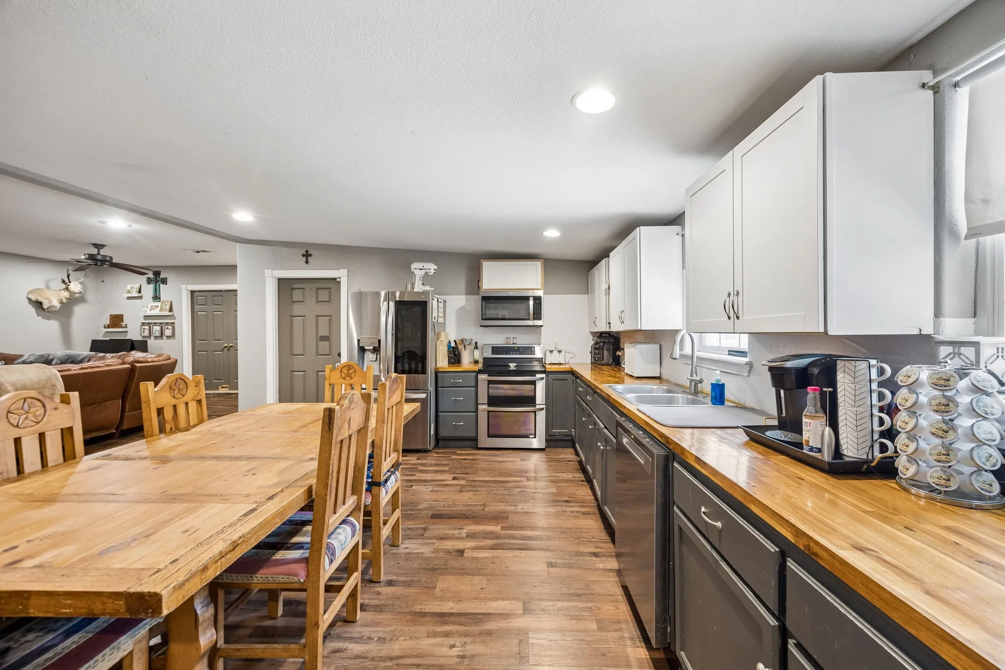 Open-concept kitchen and dining area featuring wood-finish flooring, light gray upper cabinetry, dark gray lower cabinetry, and wood countertops