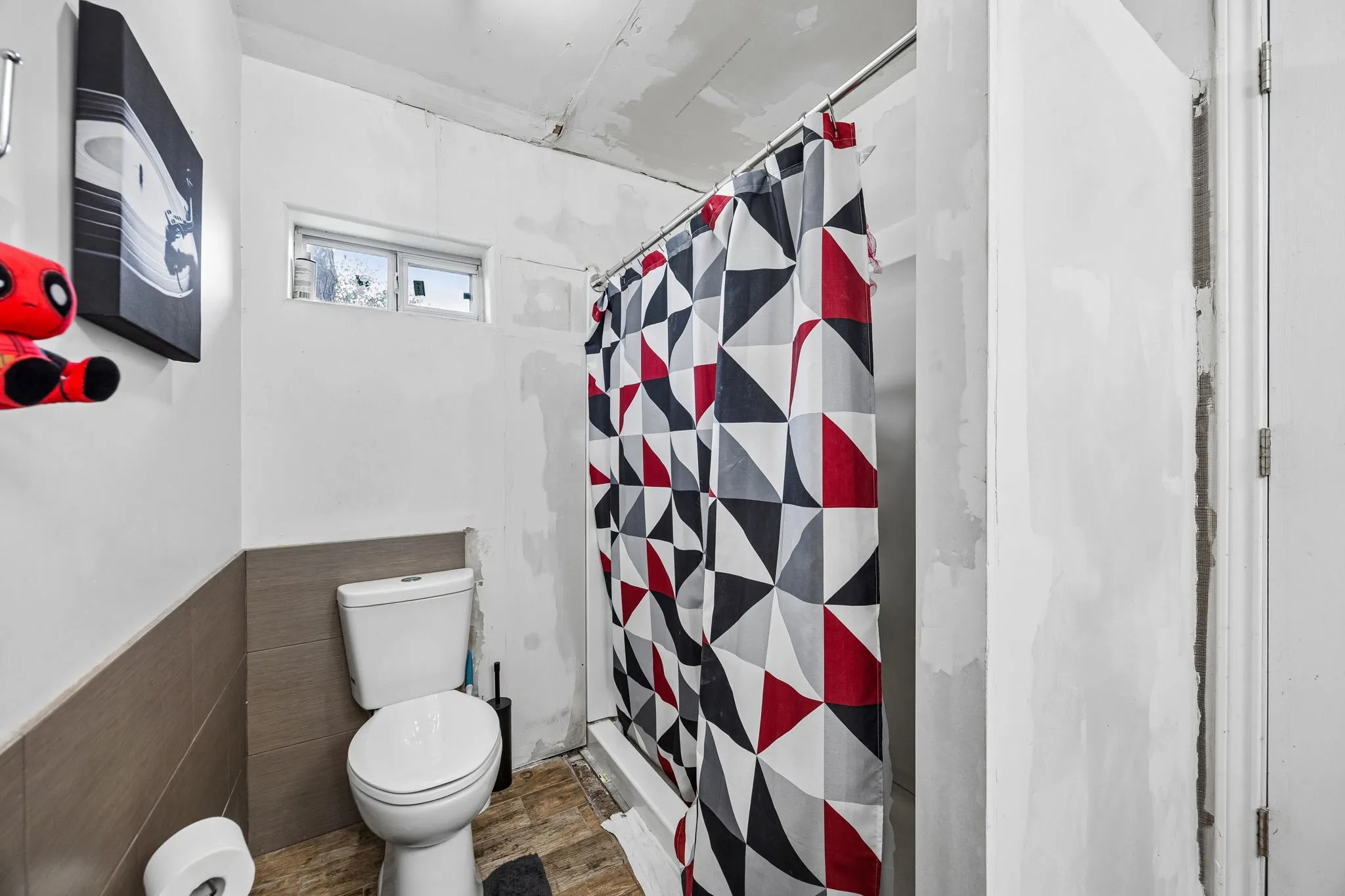 Bathroom featuring a white toilet, partially tiled walls, a window, and a shower area