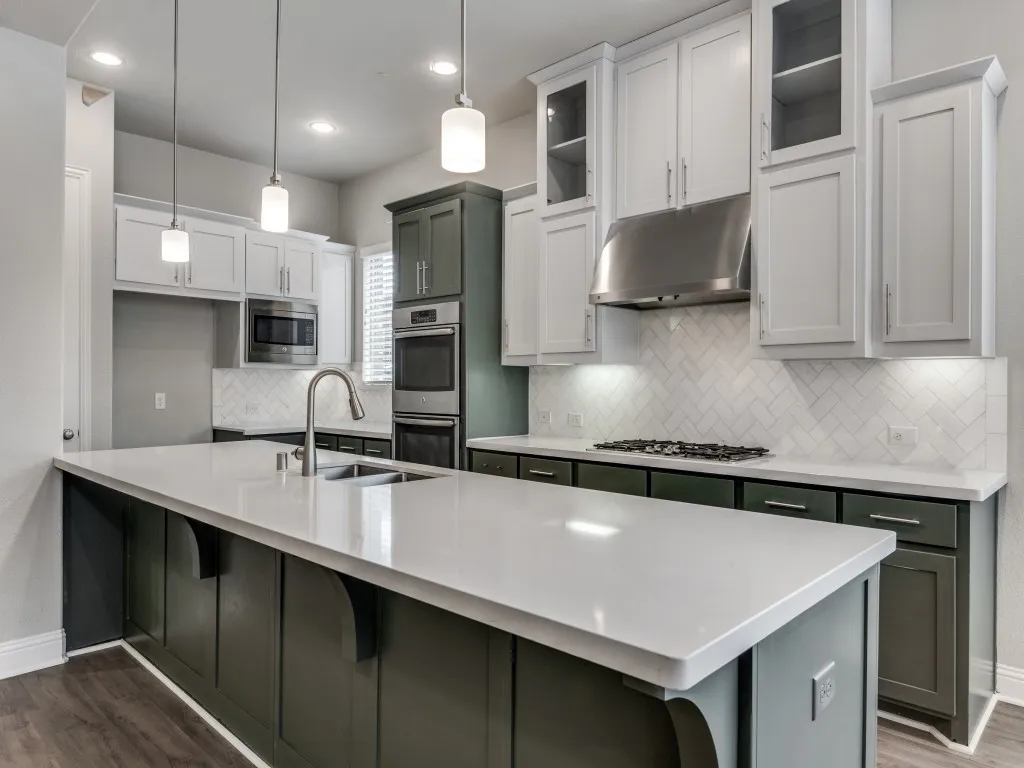 Kitchen featuring a central island with a light-toned countertop and sink, two-tone cabinetry, stainless steel appliances, a herringbone tile backsplash, and wood-finish flooring