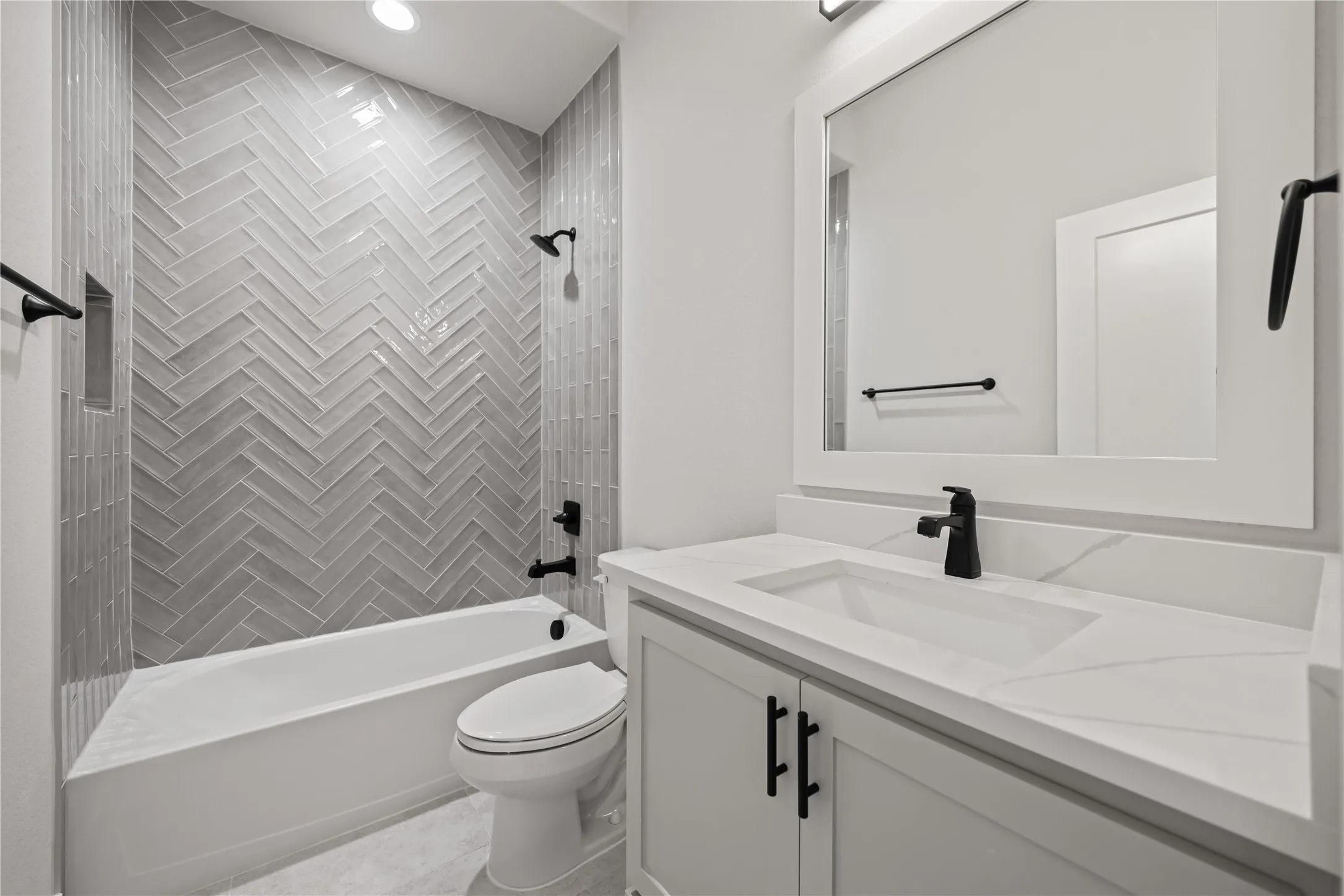Bathroom featuring a herringbone-patterned tile shower surround, a built-in shower niche, a white soaking tub, and a vanity with a white countertop and integrated sink