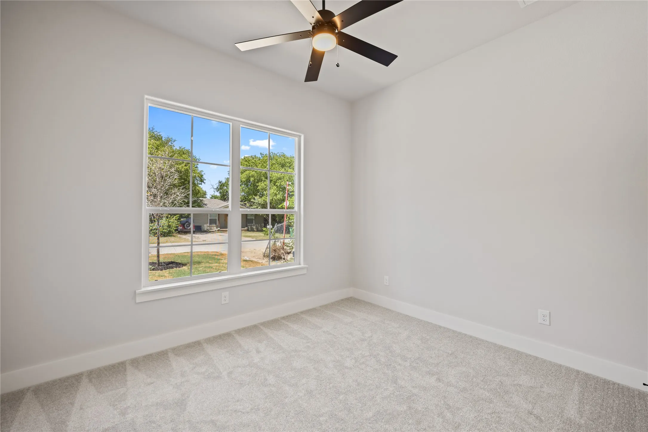 Bright interior room featuring a large window with white trim, light gray carpet, and a ceiling fan with integrated lighting