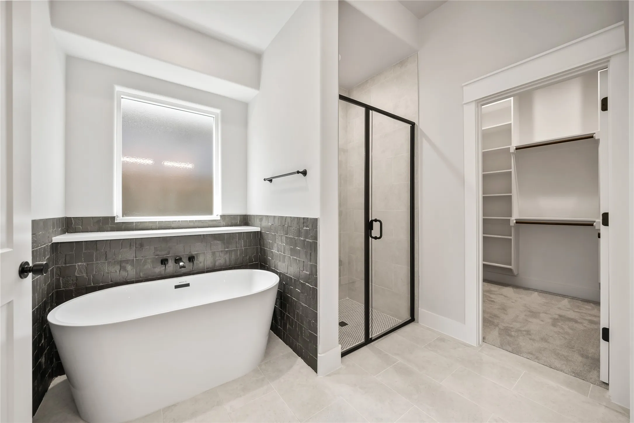 Bathroom featuring a freestanding soaking tub with matte black fixtures, a walk-in shower with a black-framed glass enclosure, and light-toned tile flooring