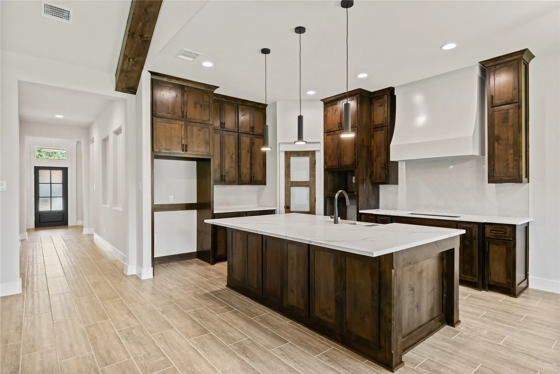 Spacious kitchen featuring dark wood cabinetry, white countertops, and a central island with a sink and pendant lighting