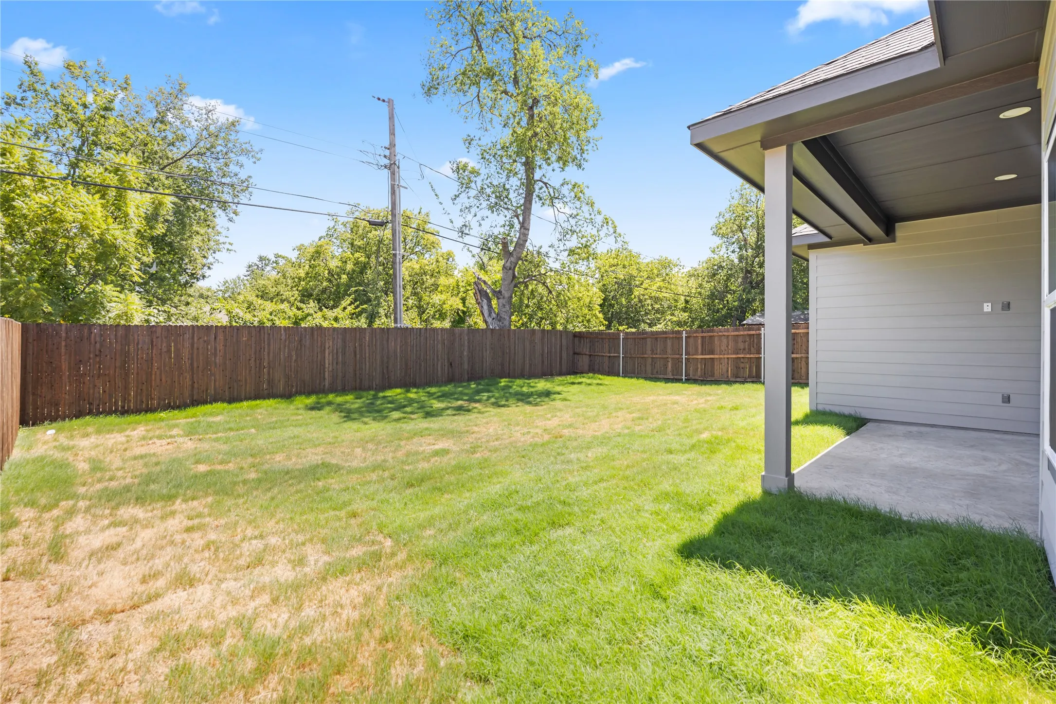 Expansive backyard featuring a privacy fence, a concrete patio, and a covered patio area with recessed lighting