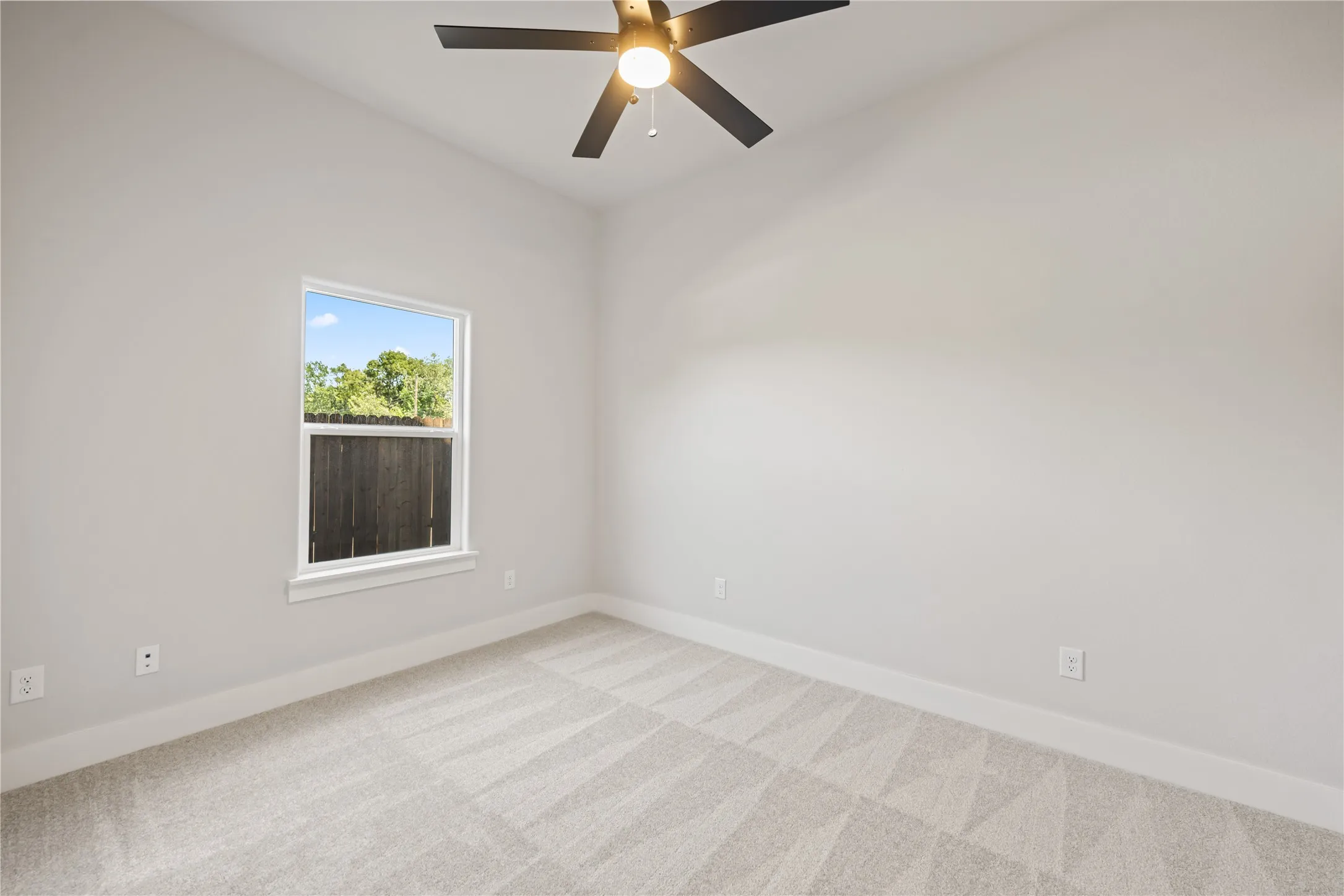 Bright room with a window providing natural illumination, ceiling fan, neutral wall tones, and patterned carpet flooring
