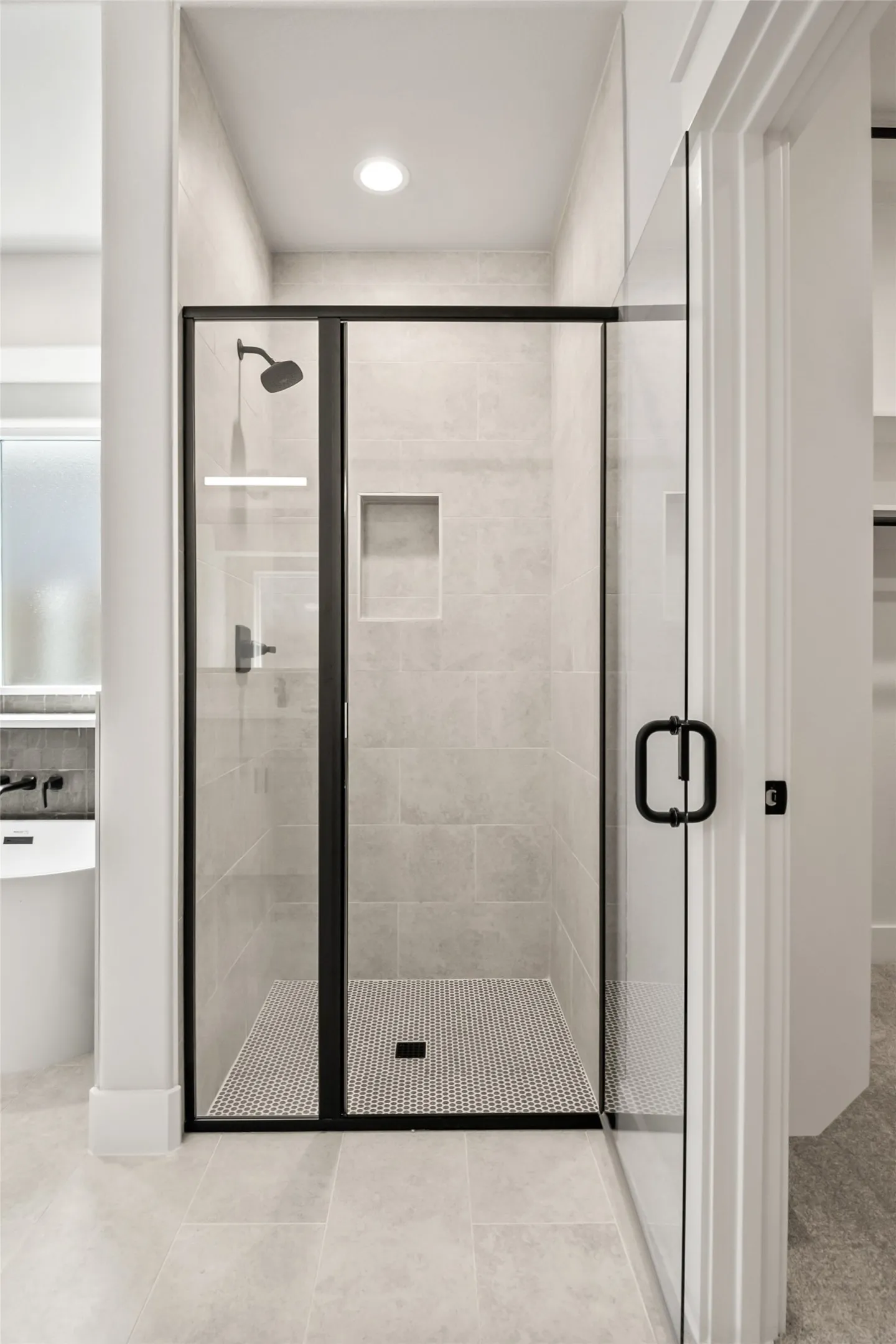 Spacious walk-in shower featuring a frameless glass enclosure with matte black trim, subway tile walls, a built-in shower niche, and a contrasting penny tile floor